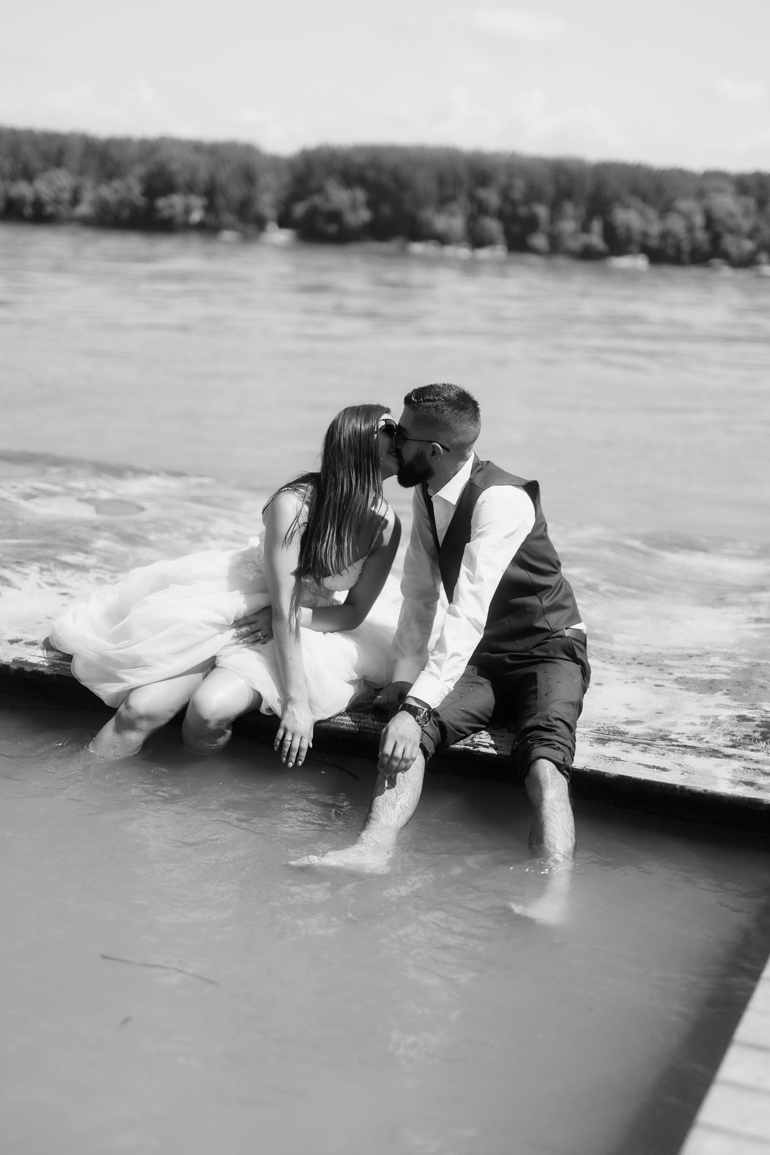 A couple in formal attire lying together in the sand as ocean waves wash over them during a romantic beach photoshoot.