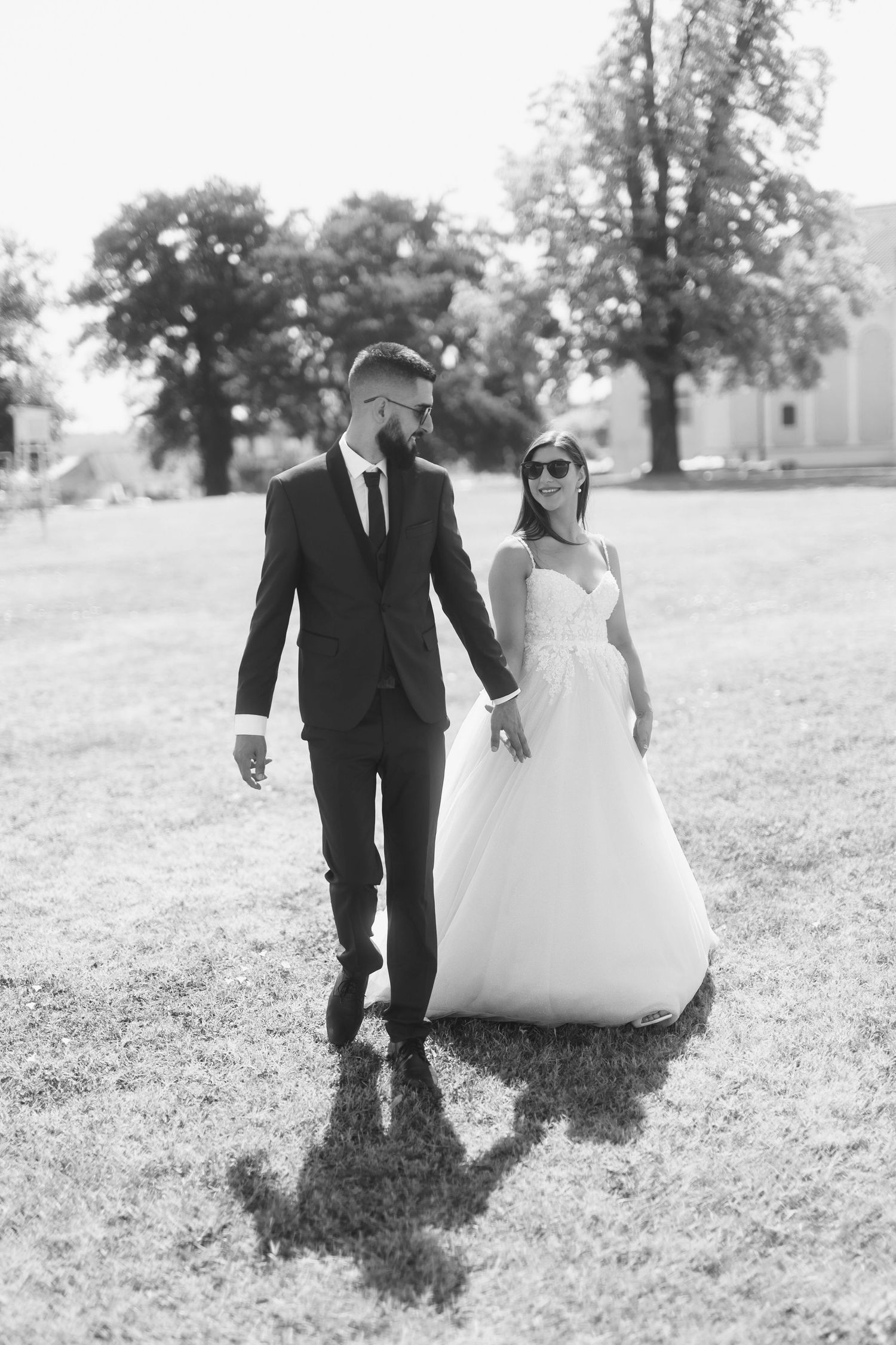 A couple in wedding attire walks together on a grassy lawn in black and white photography.