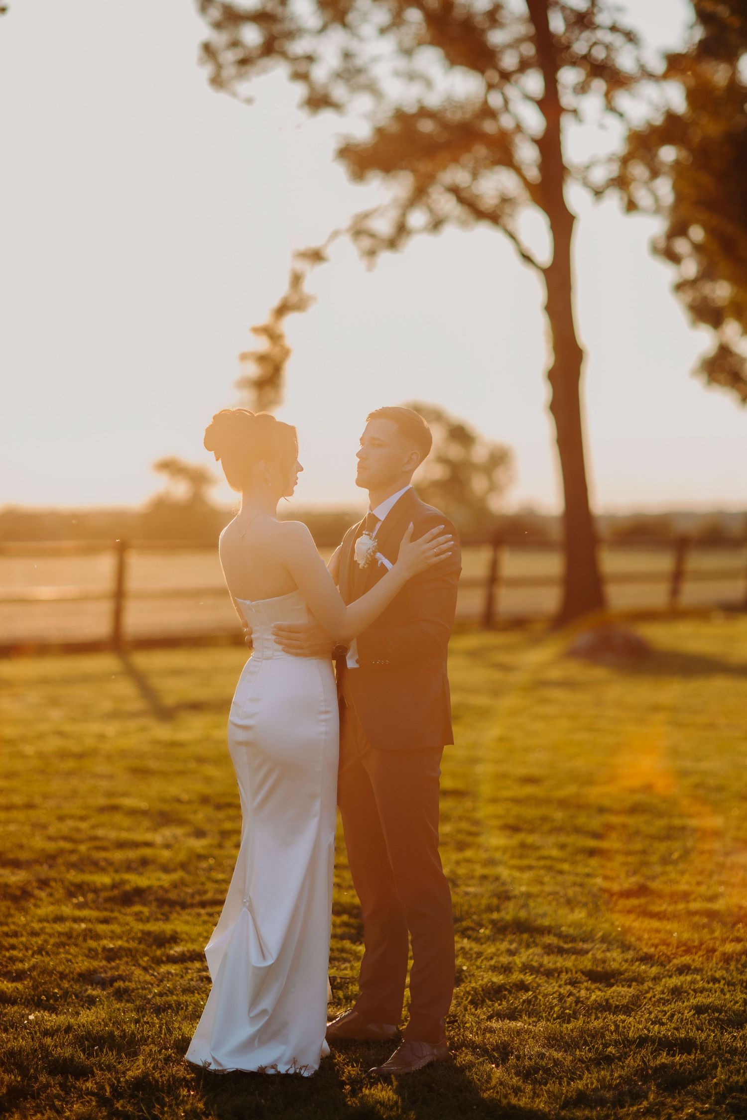 Silhouetted couple embracing in golden sunlight on grassy hill during sunset photoshoot.