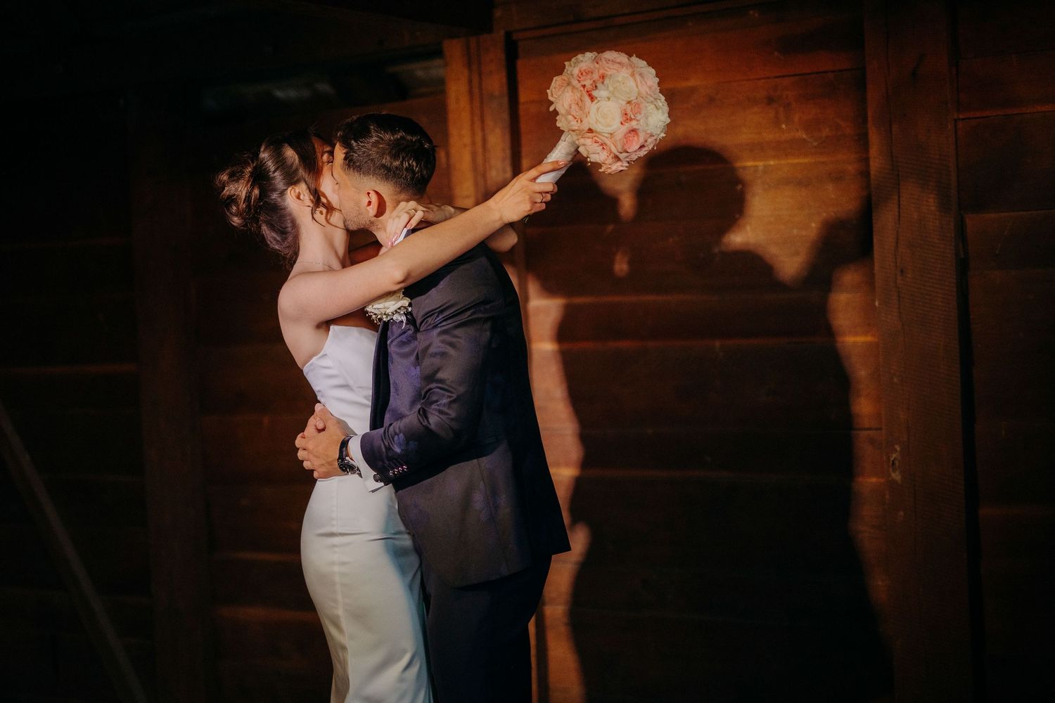 A newlywed couple dances closely together in an intimate moment on a rustic wooden dance floor at their reception.