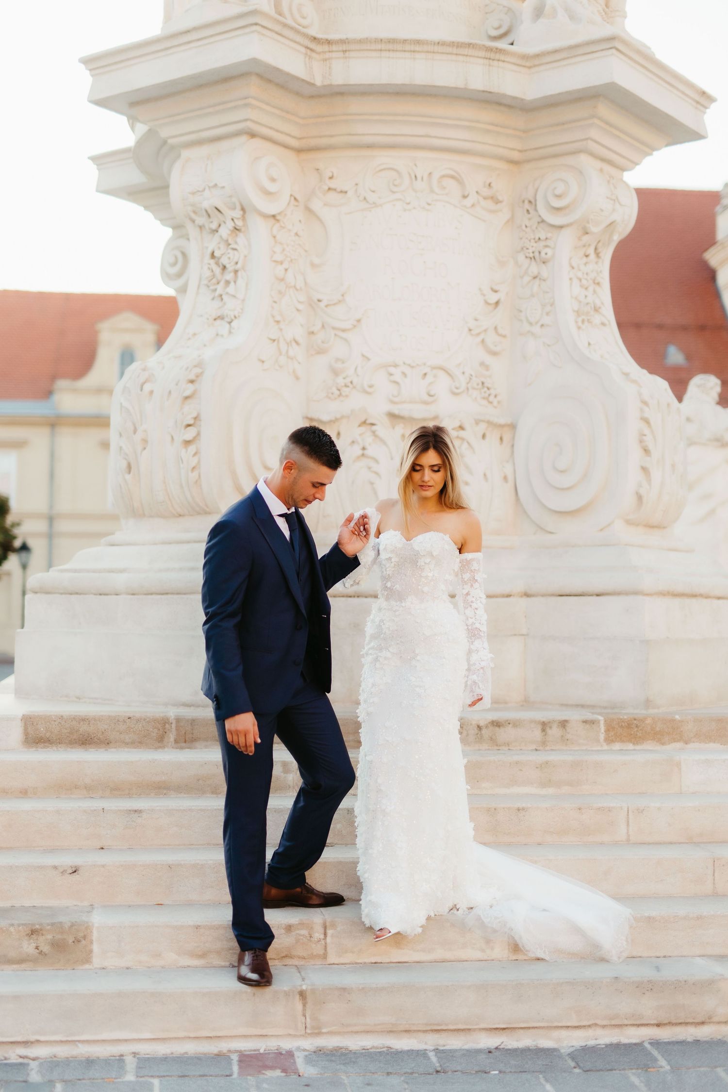 Wedding couple descending ornate stone steps in elegant attire.