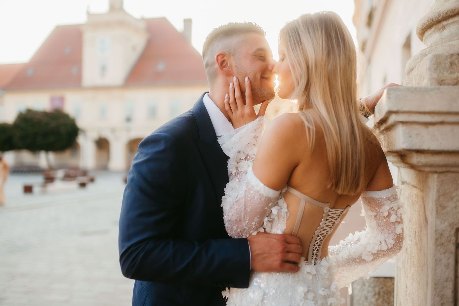 A romantic wedding couple sharing a kiss by rustic stone pillars during golden hour.