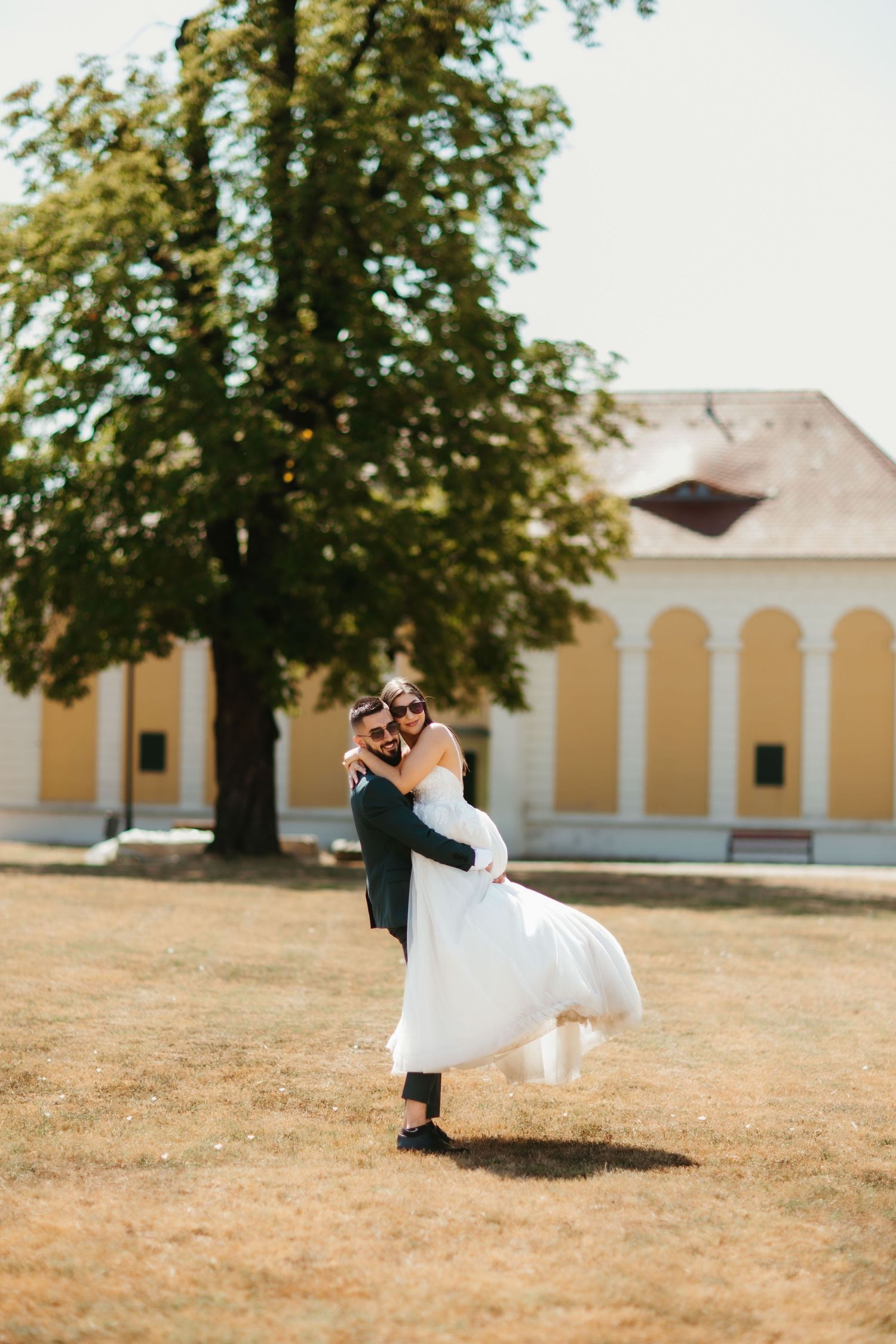 A couple sharing an intimate moment on their wedding day outside a yellow building with arches on a sunny summer day.