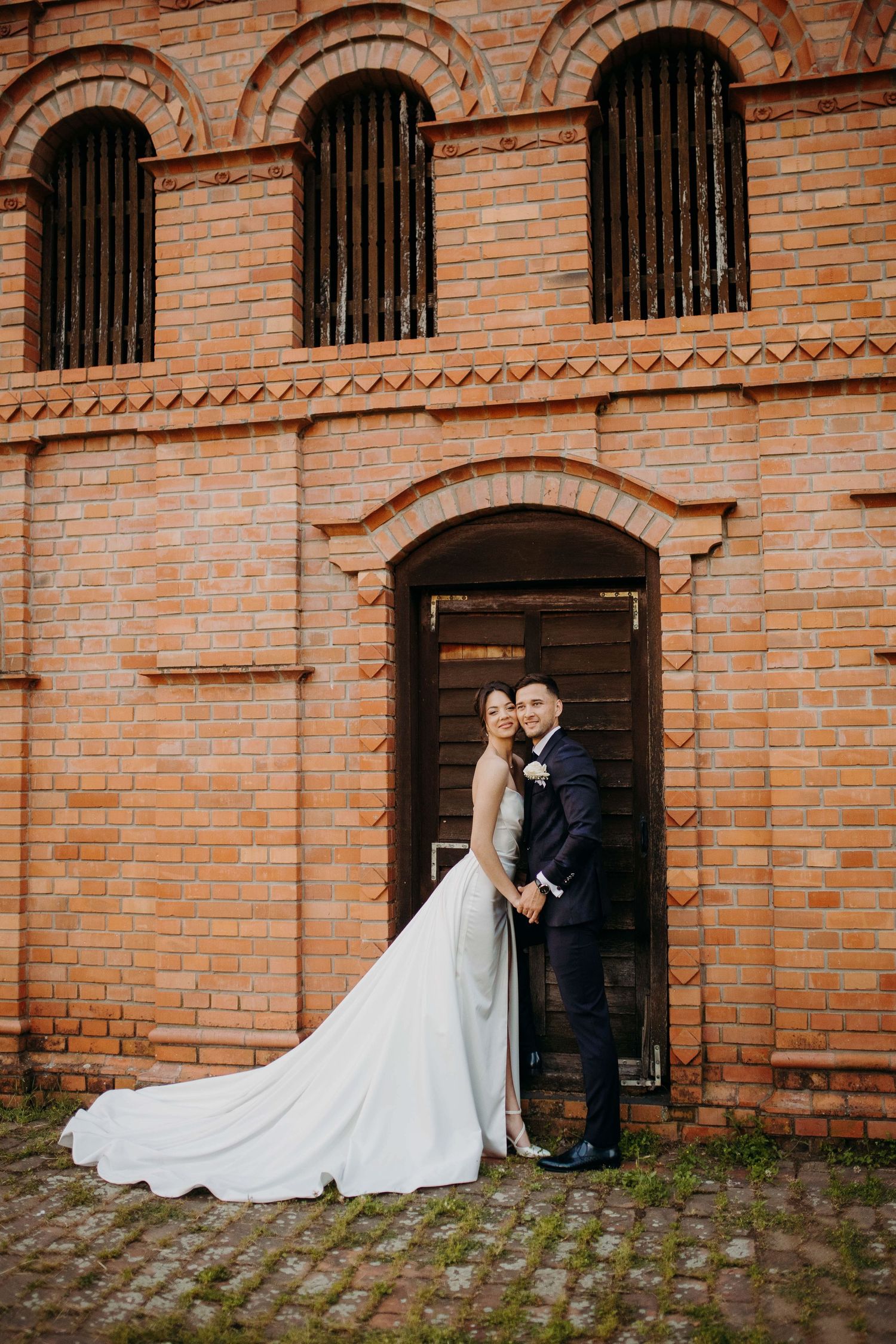 A couple stands in a rustic brick doorway during their wedding, with the bride wearing a long white train gown.