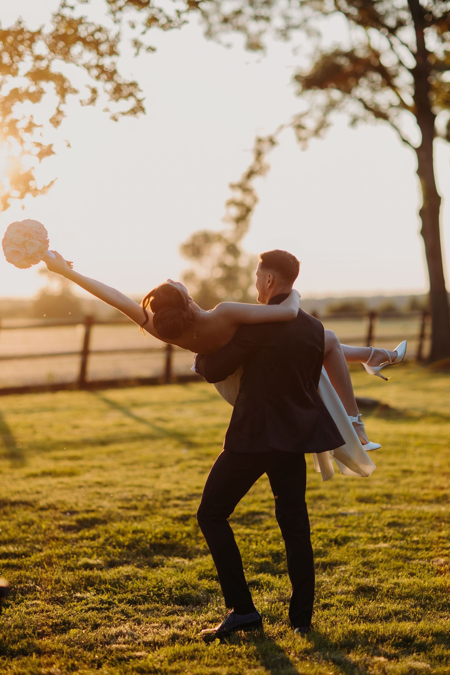 Two people sharing a joyful moment at sunset in a grassy field, with one holding the other in a playful dip pose.