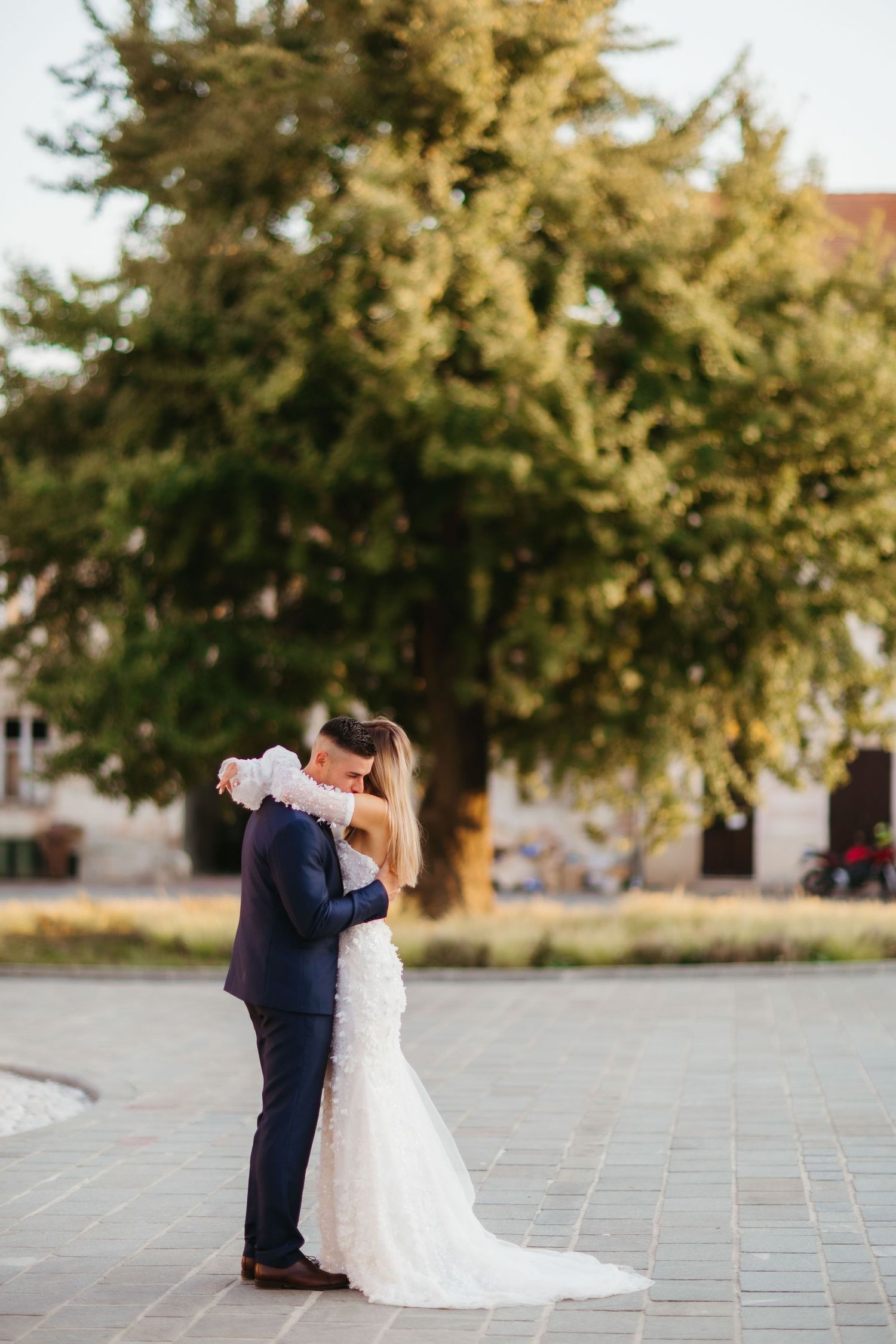 Elegant wedding portrait with couple embracing in front of large tree.