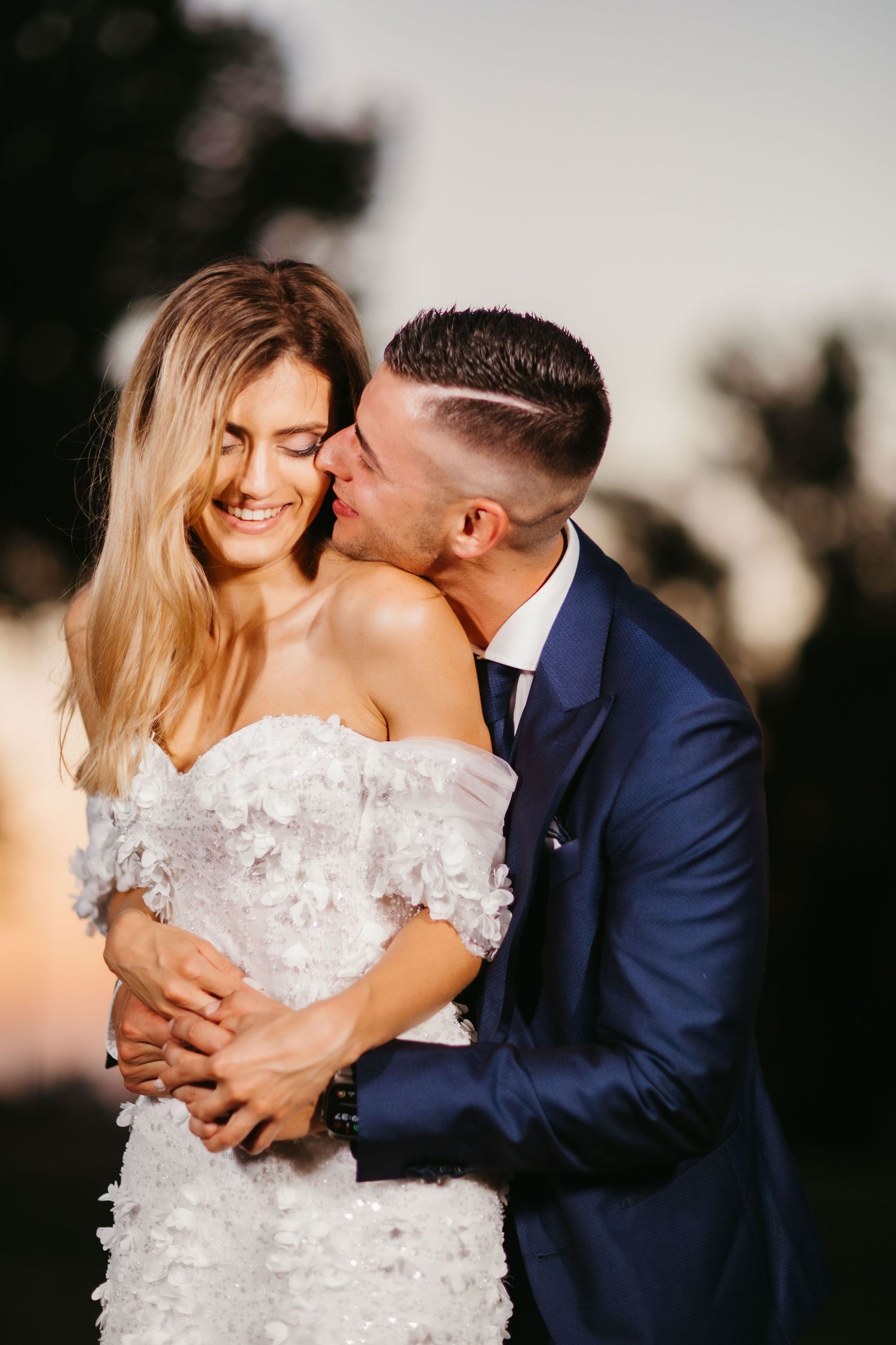 Romantic sunset wedding photo showing tender moment between couple in elegant formal attire.