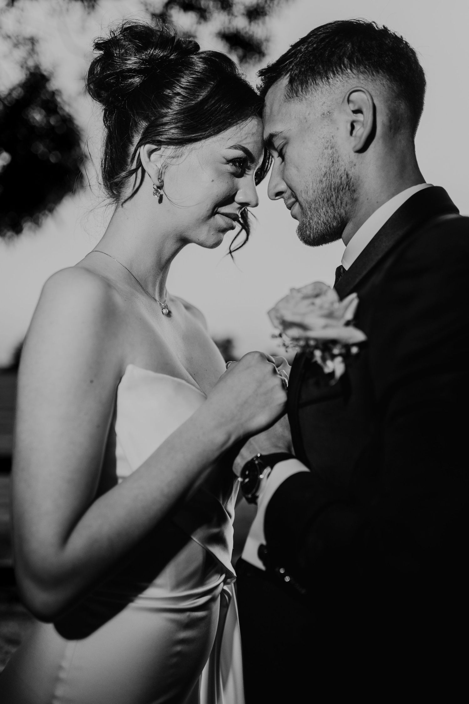 Black and white intimate wedding photo of a couple sharing a tender moment with bride in strapless gown and groom in suit.