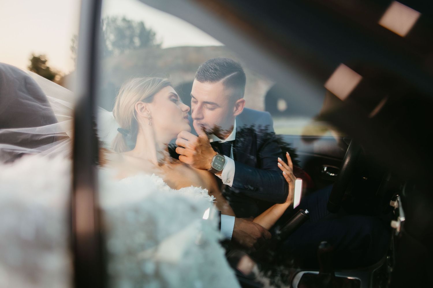Tender wedding moment captured through car window glass.