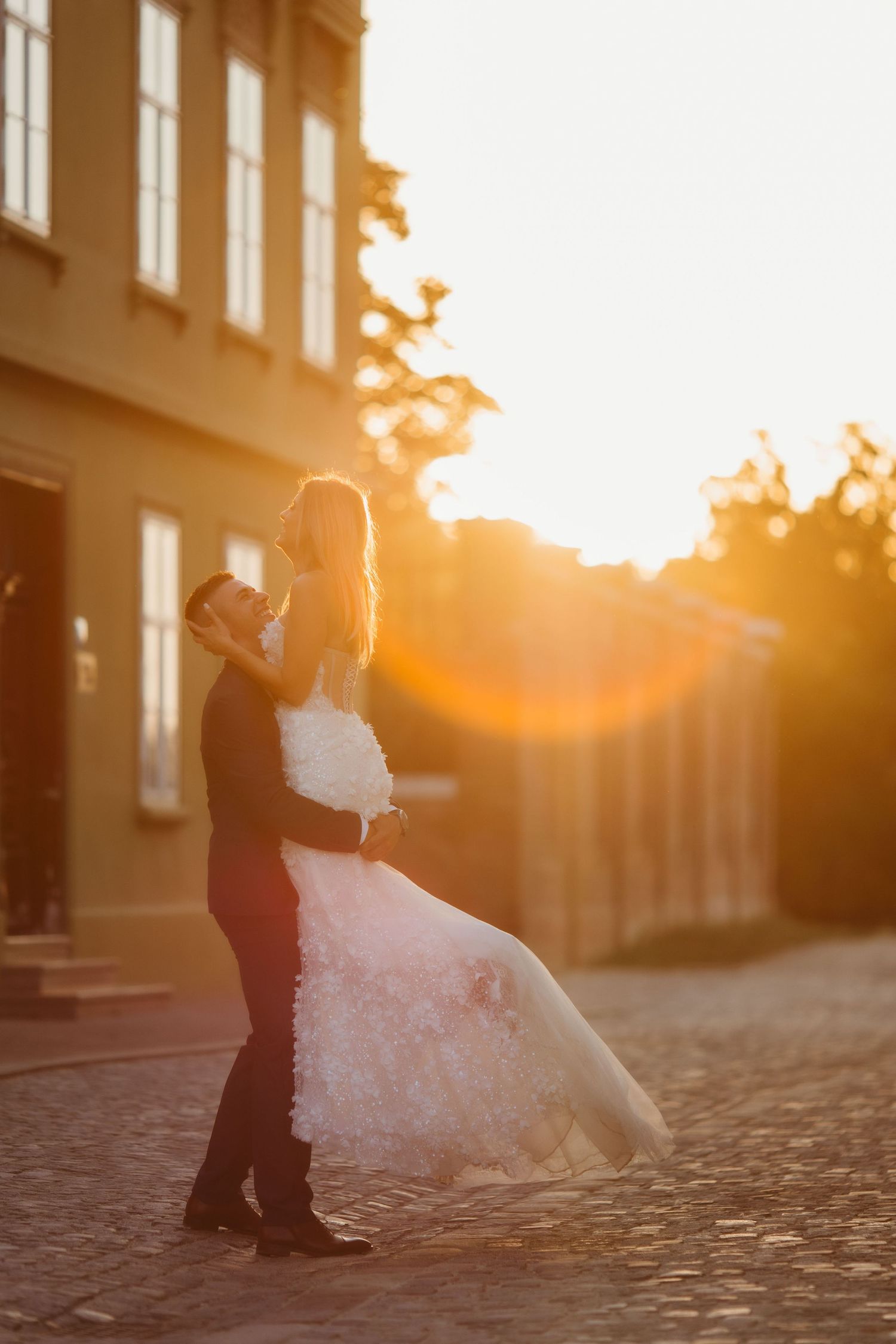 Romantic sunset wedding photo with couple silhouetted against historic building backdrop.