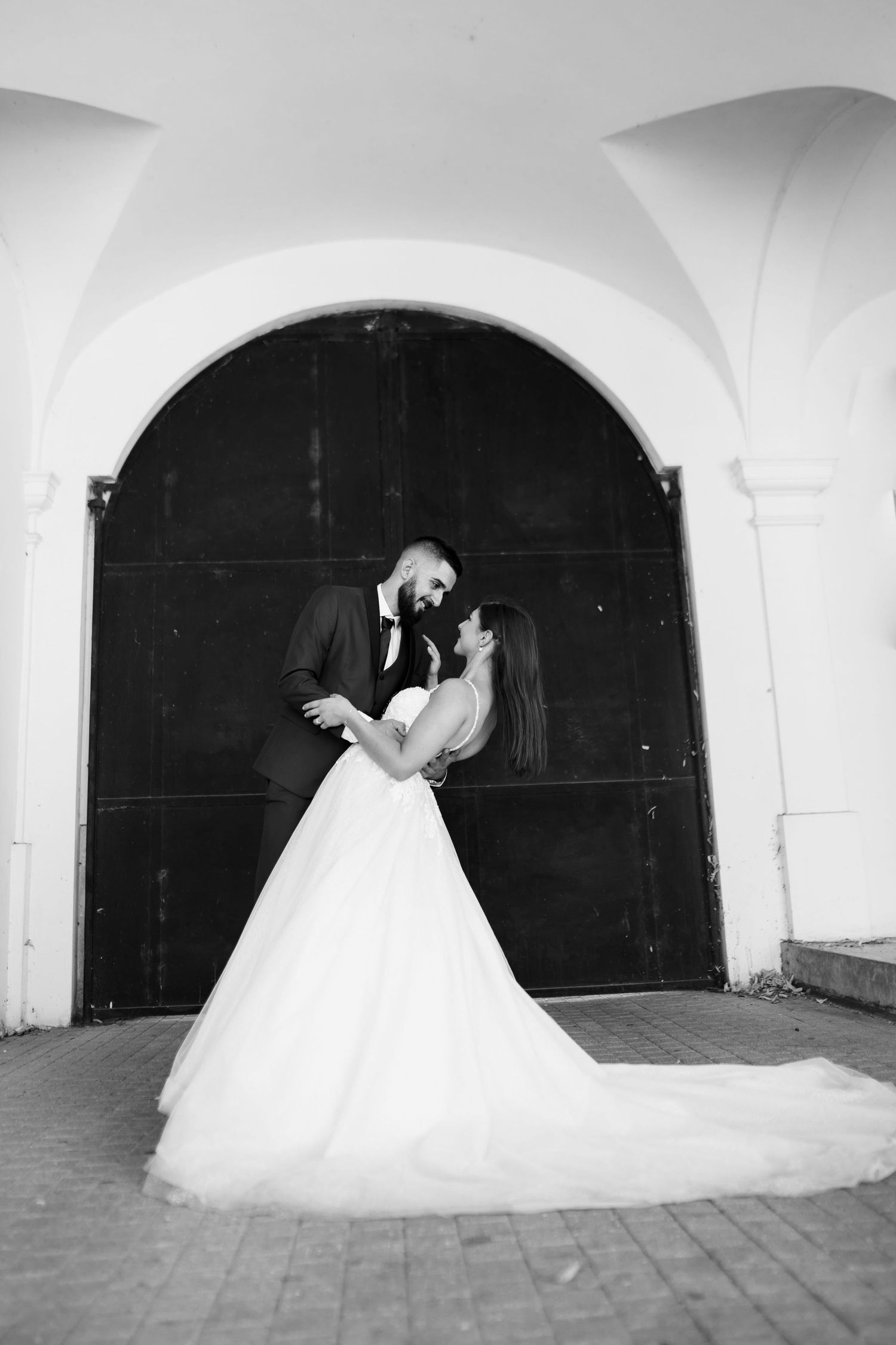 Black and white wedding photo of a couple embracing under an arched doorway, bride in flowing white gown.
