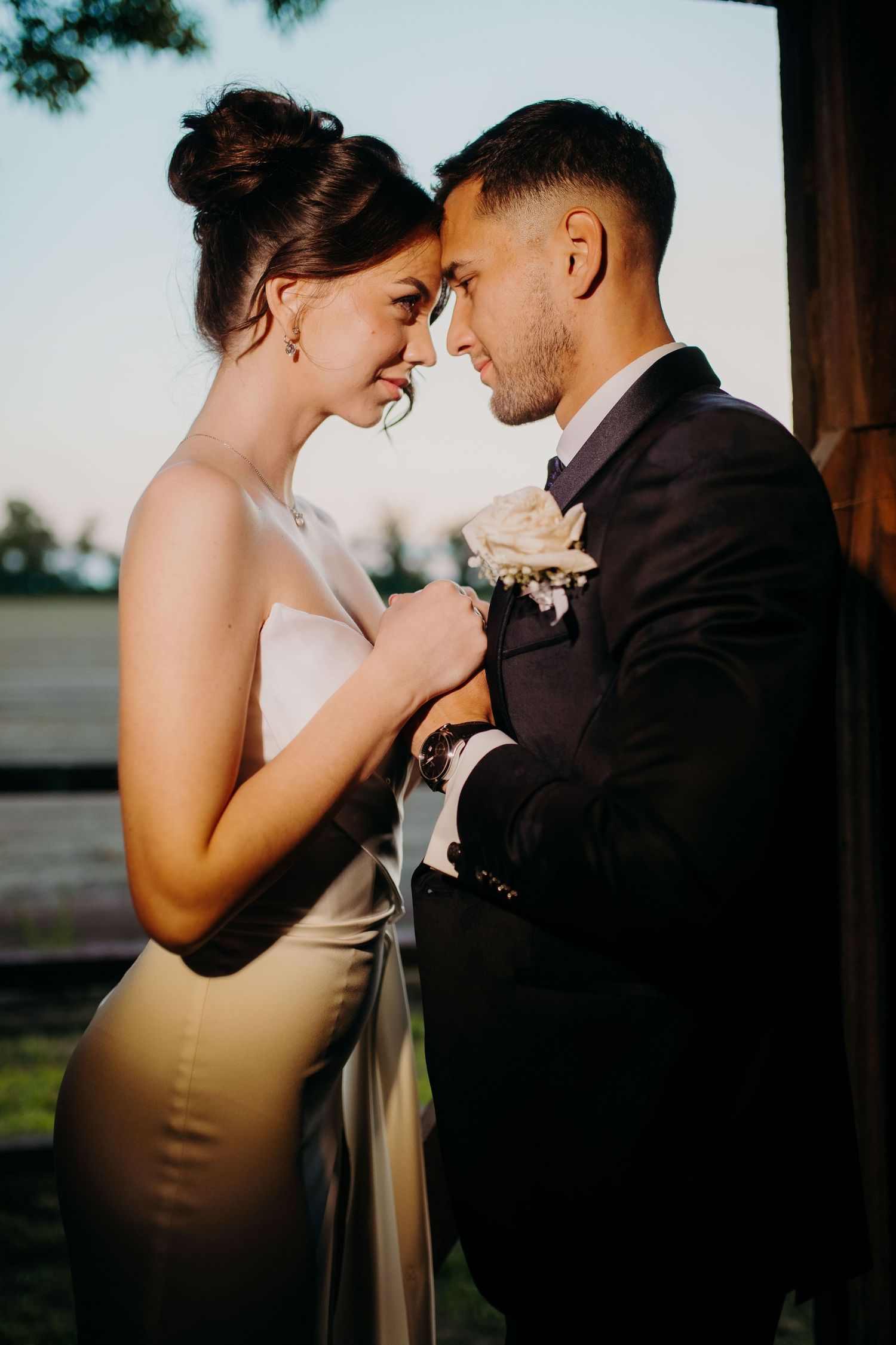 Intimate wedding moment captured between newlyweds sharing tender embrace at sunset outdoors.