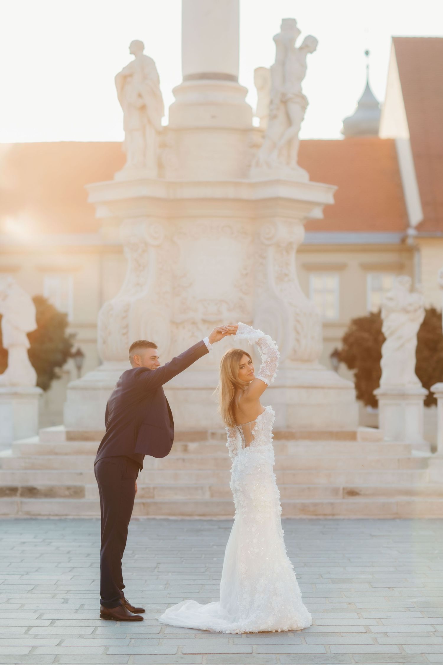 Wedding couple dancing in front of baroque monument at golden hour.