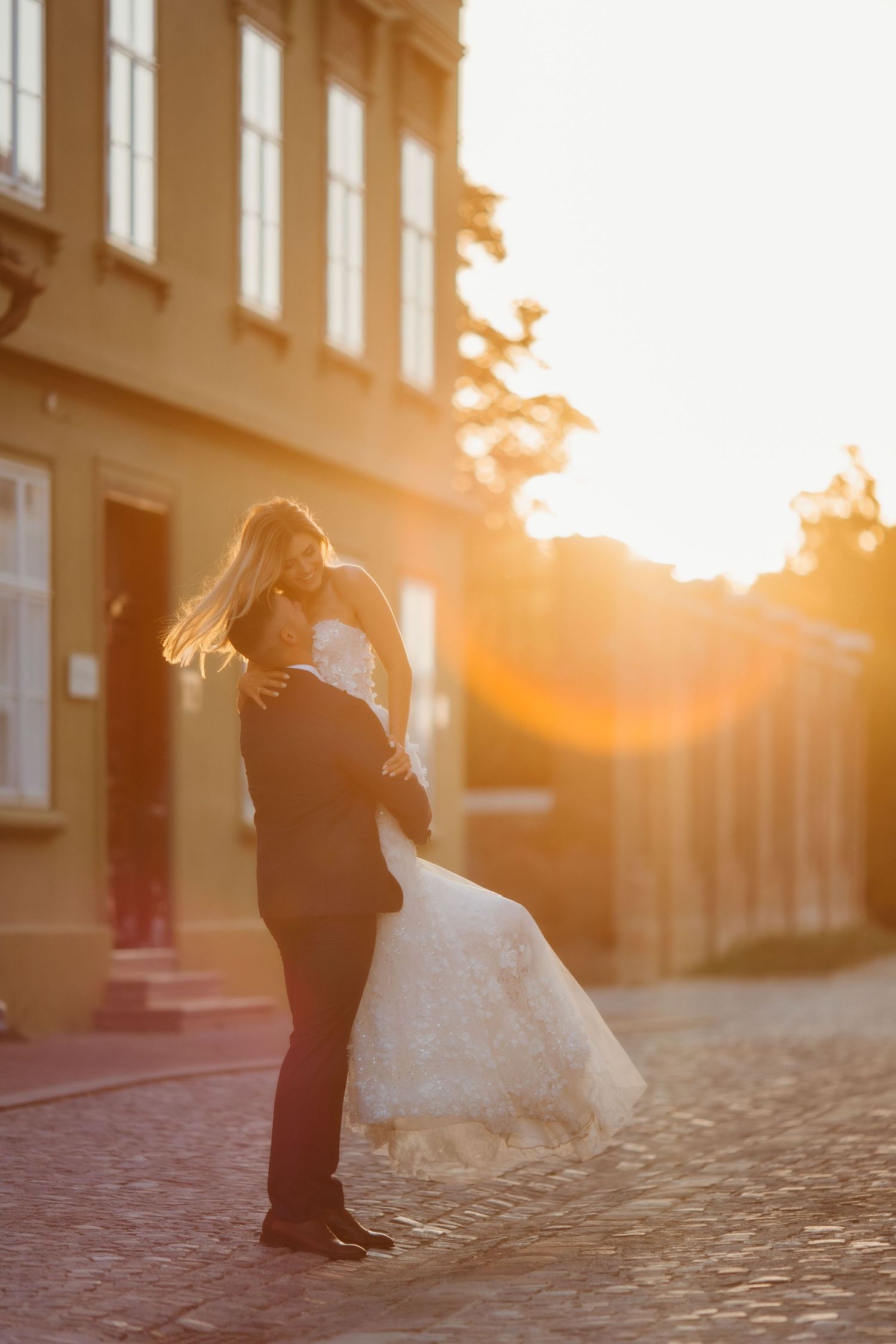 A wedding couple in an intimate embrace on a European cobblestone street during golden hour.