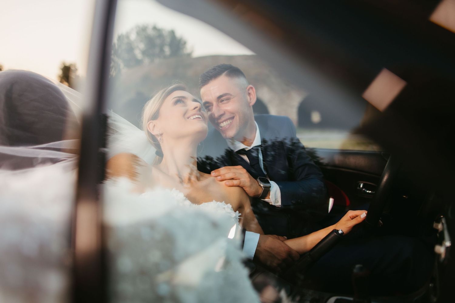 Romantic candid moment between newlyweds through car window.