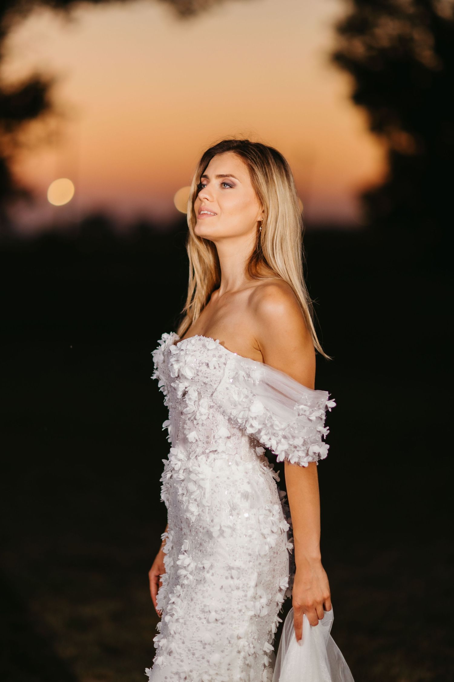 An elegant off-shoulder wedding dress with floral details photographed during golden hour.