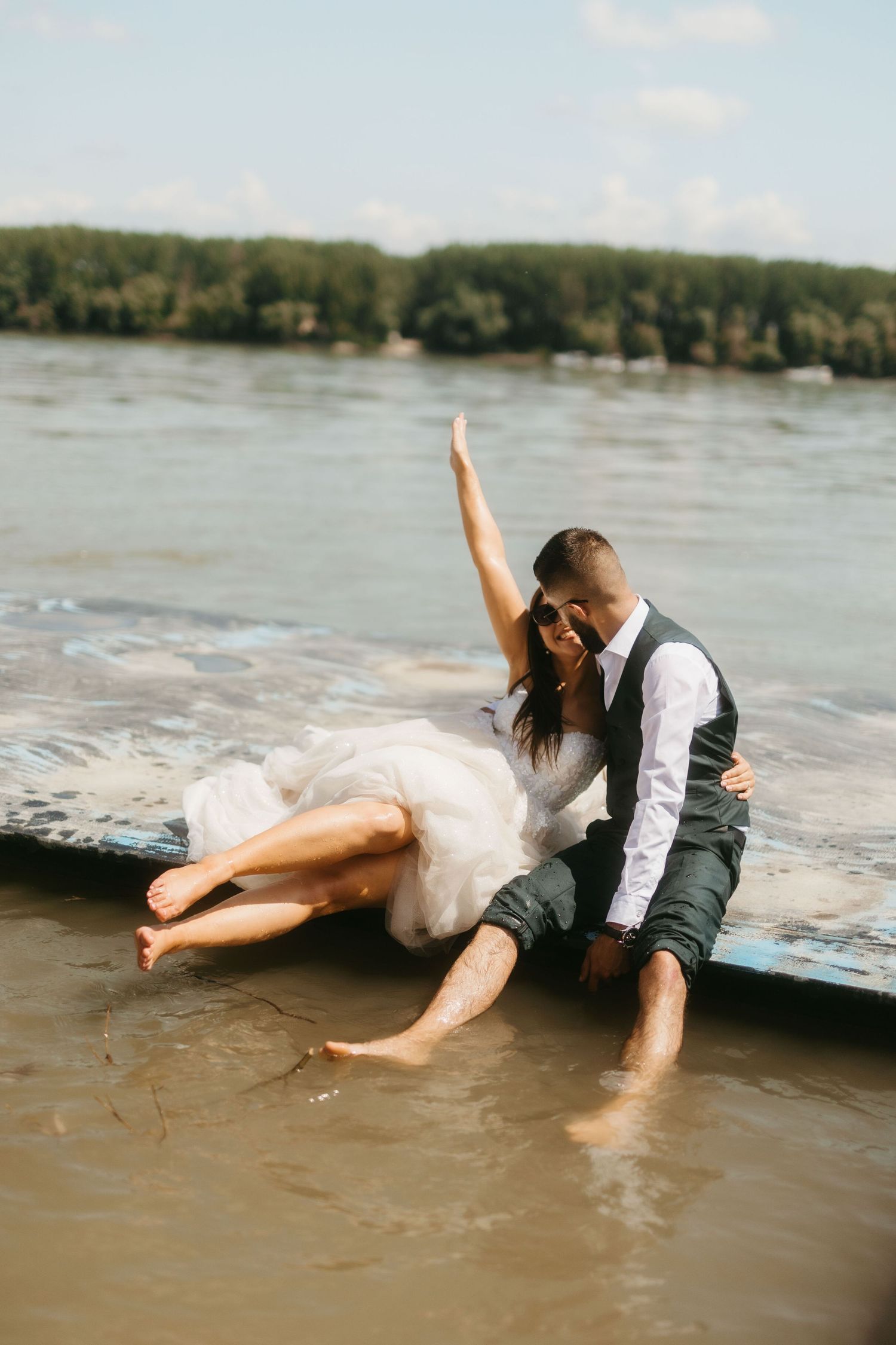 A romantic couple lies on a wooden dock by the water in a playful summer moment.