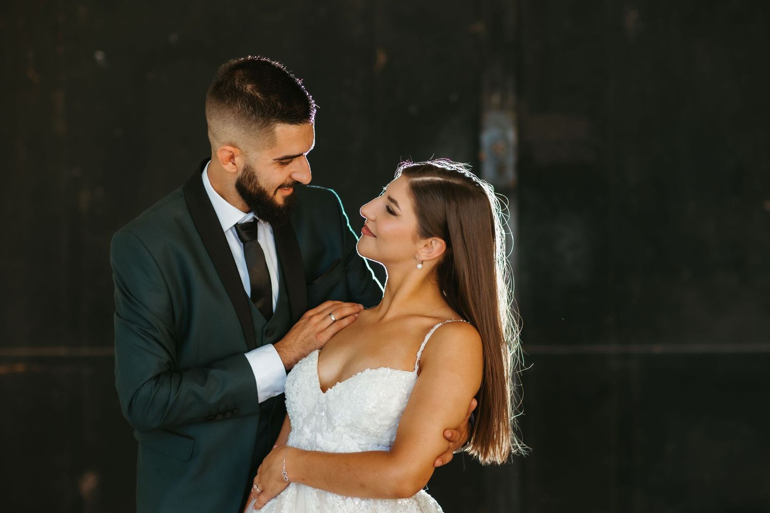 A bride in a white dress and groom in dark suit share an intimate moment during their wedding photoshoot.