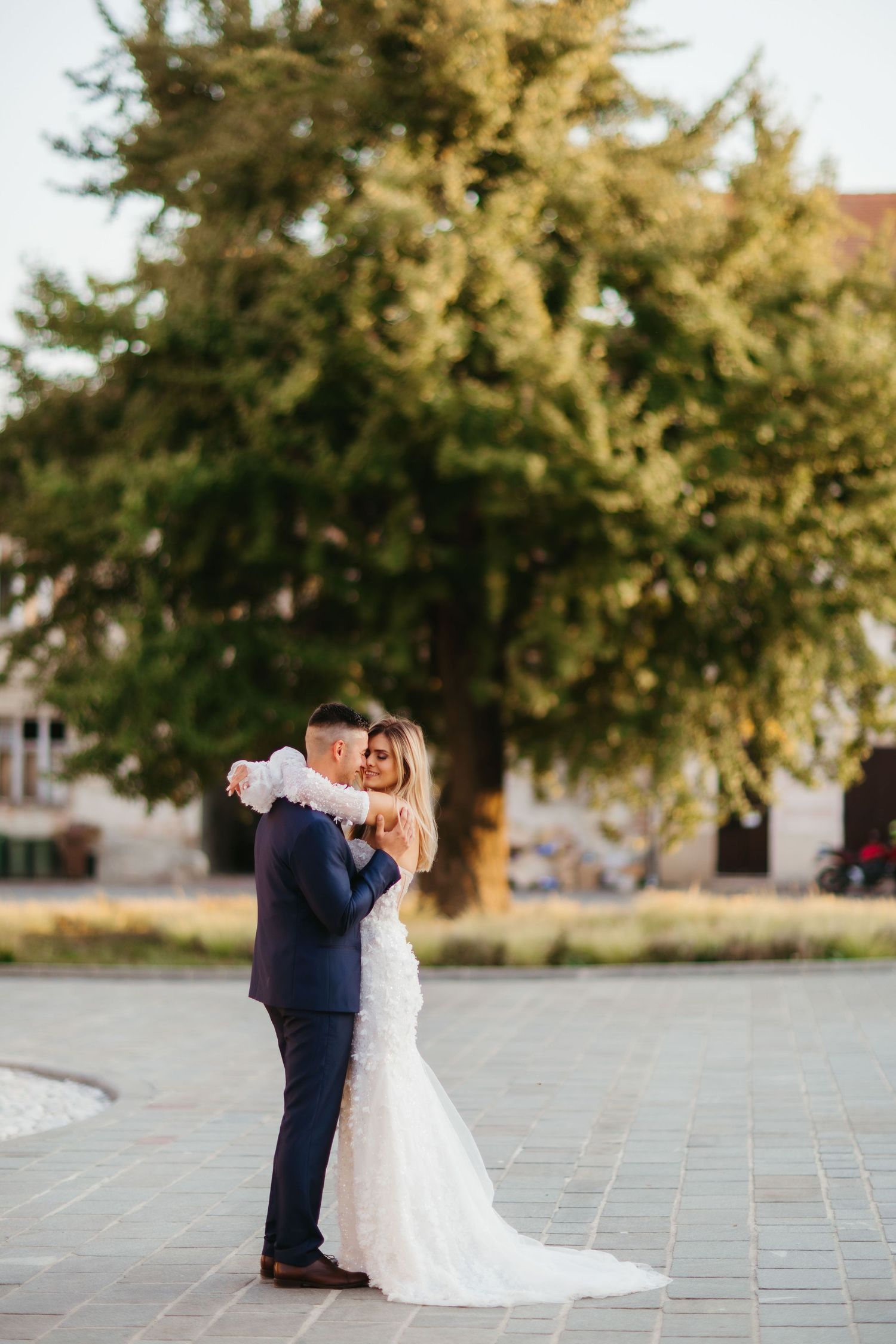 Wedding couple sharing tender moment on stone plaza with tree in background.