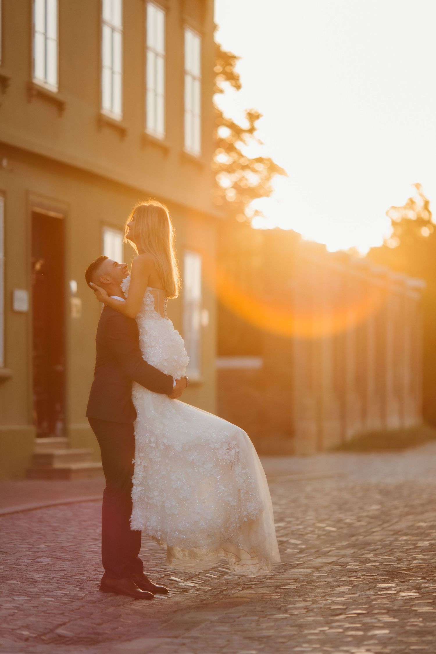 A romantic sunset wedding portrait on a cobblestone street with a couple embracing against golden sunlight.
