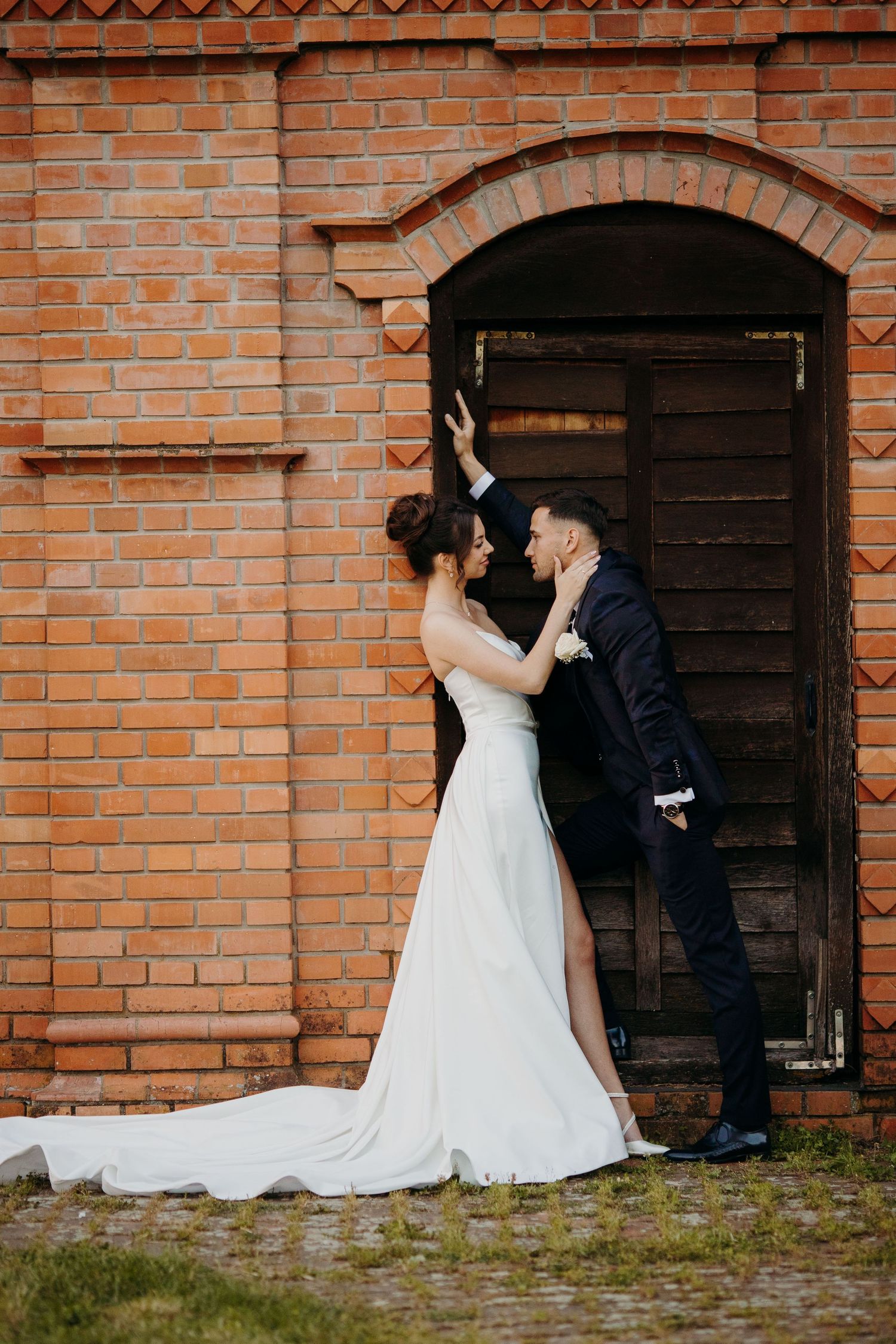 A romantic scene shows a couple in wedding attire embracing against a rustic brick wall with multiple doorway arches.