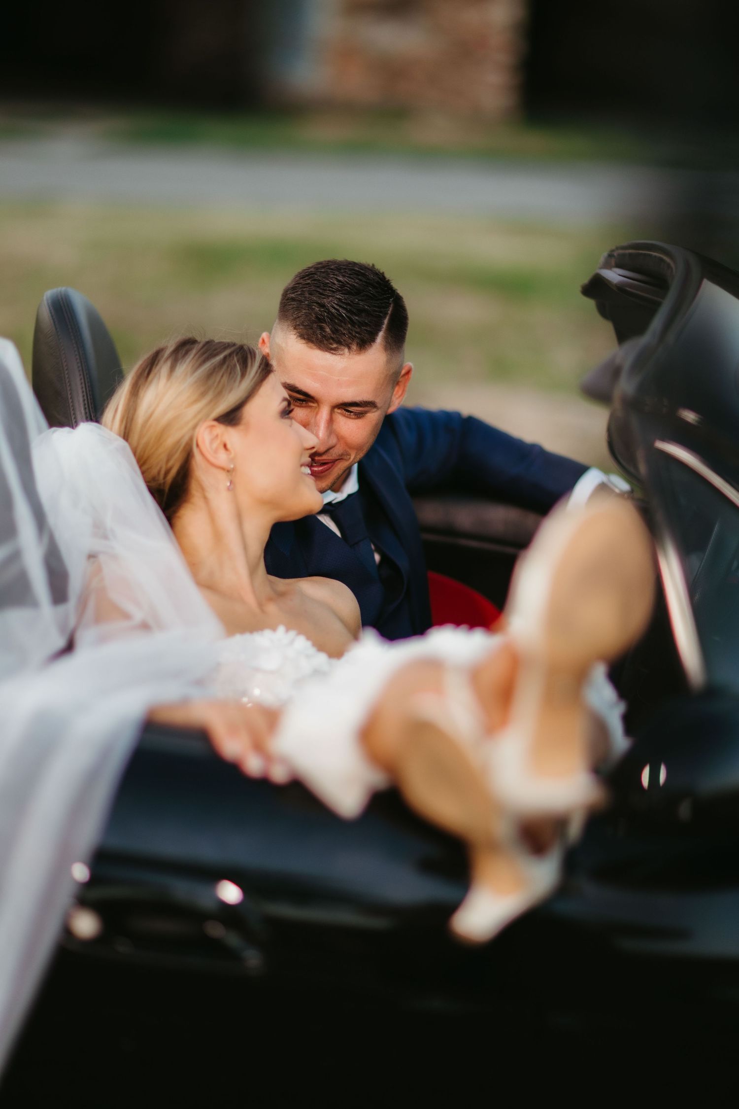 Intimate moment between newlyweds in a convertible car with flowing veil.