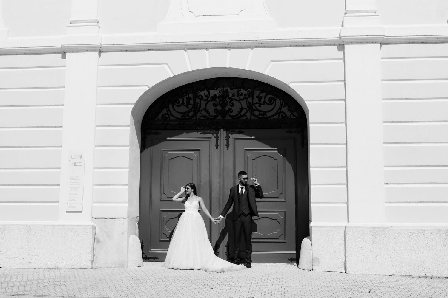 Black and white photo of a couple in formal wedding attire standing in front of a grand arched doorway.