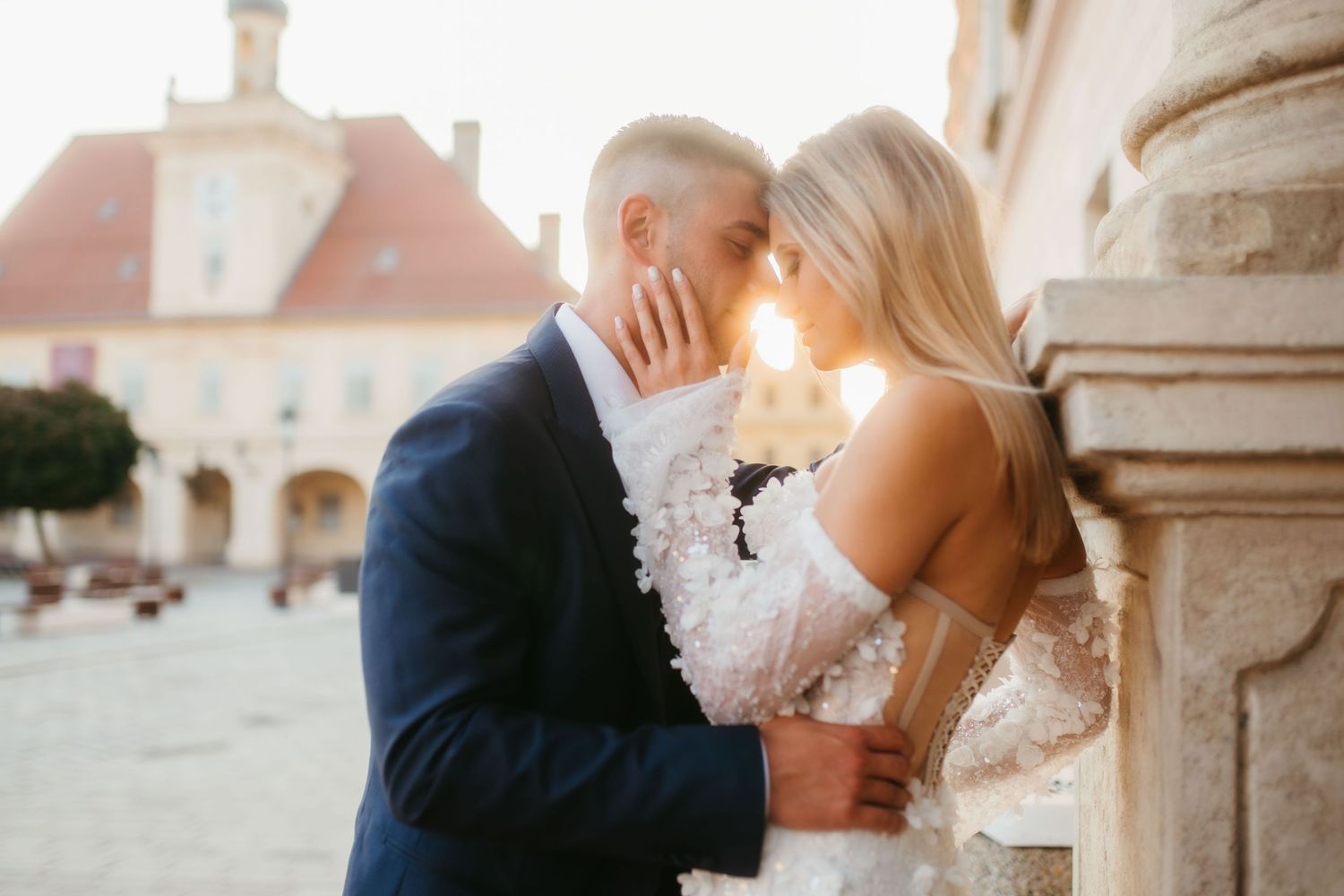 Intimate wedding moment captured against historic European architecture at sunset.