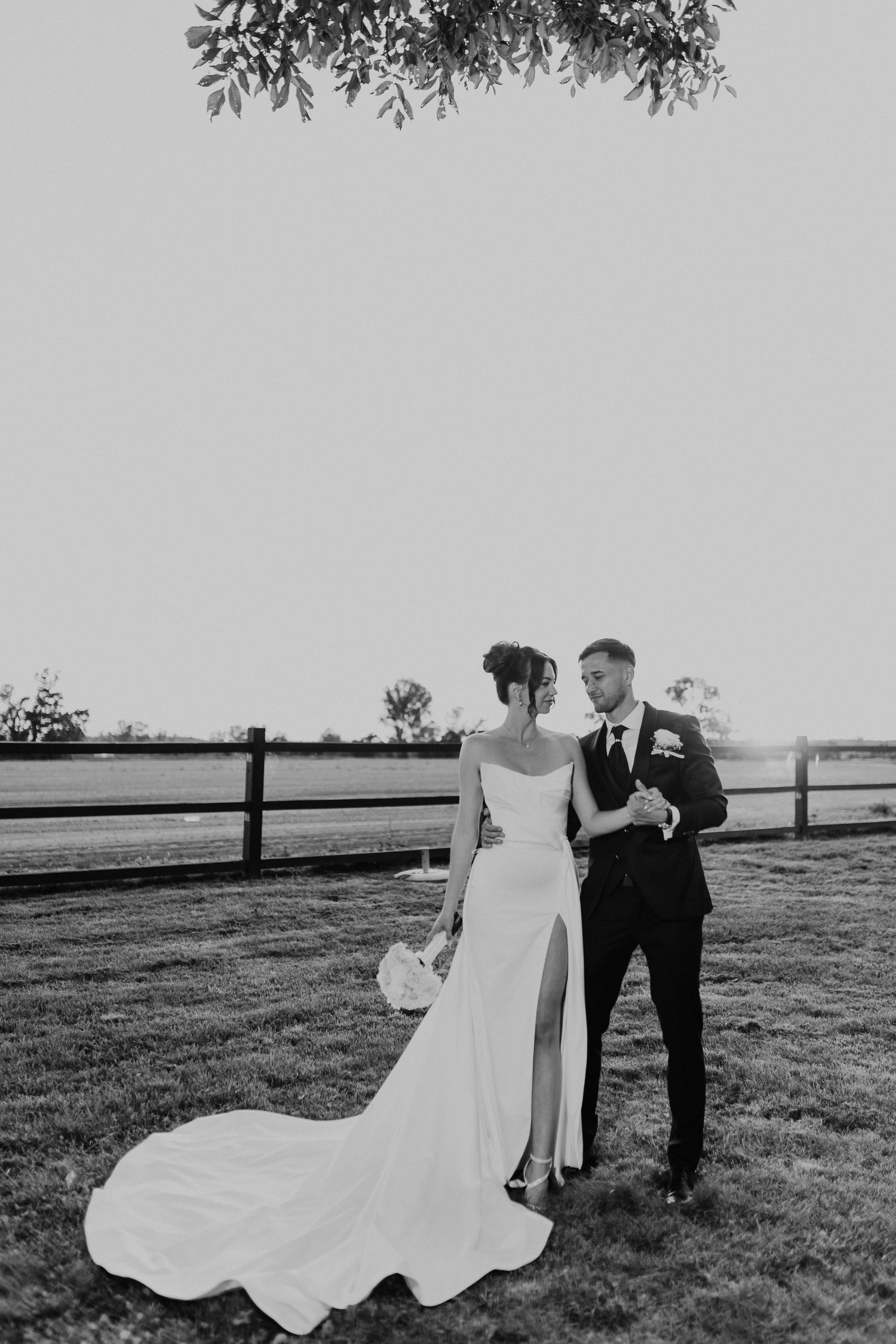 Black and white wedding photo series showing bride and groom walking and posing together in an open field with fencing.