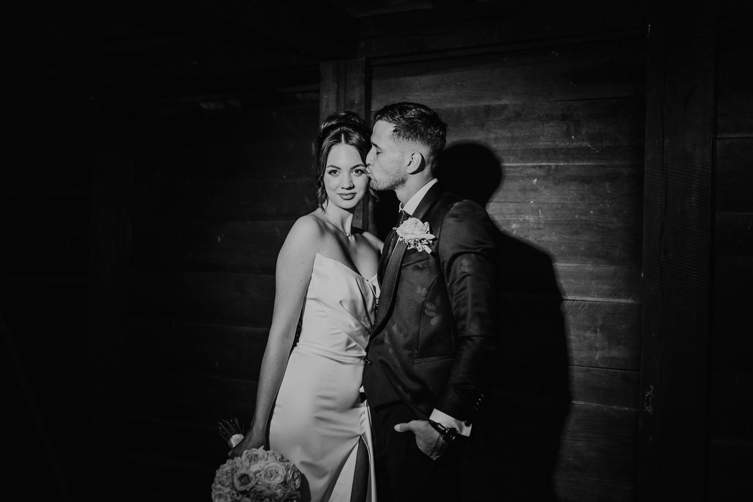 A tender black and white wedding moment captured against a rustic wooden wall backdrop.