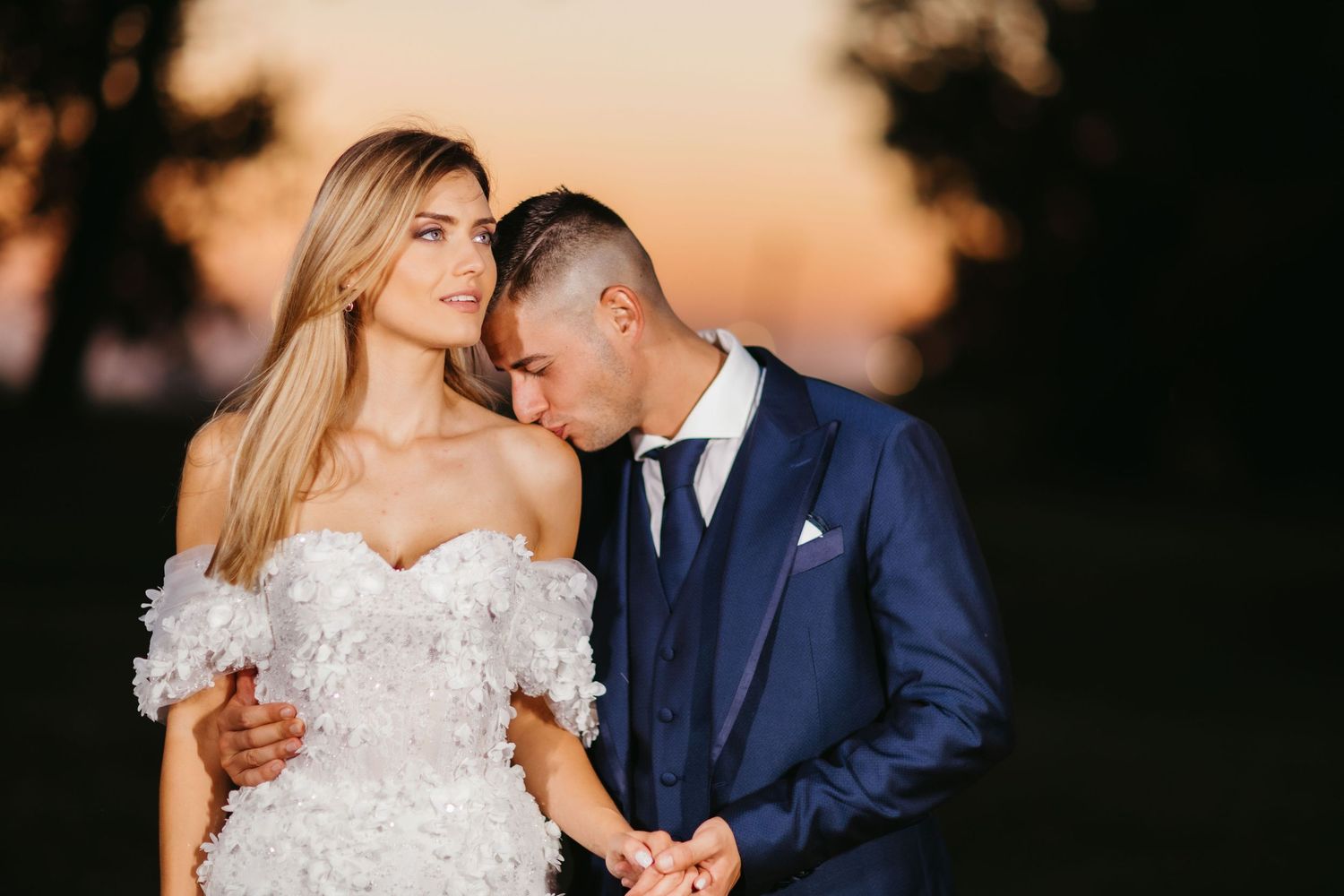Intimate wedding portrait showcasing tender moment between couple against warm sunset backdrop.