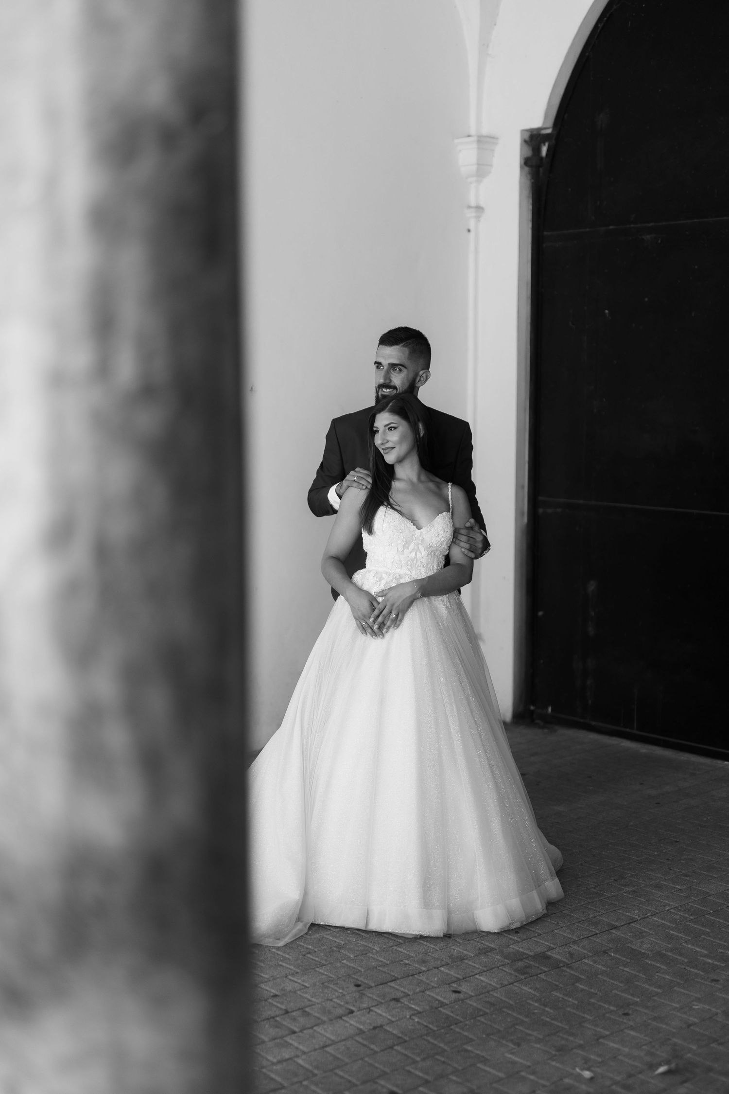 A romantic black and white wedding photo showing a couple embracing in front of an arched doorway.