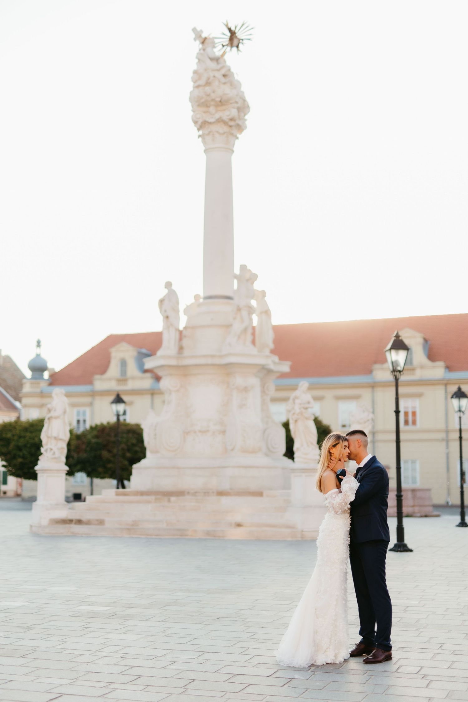 Newlyweds embrace near a grand white stone column and historic architecture.