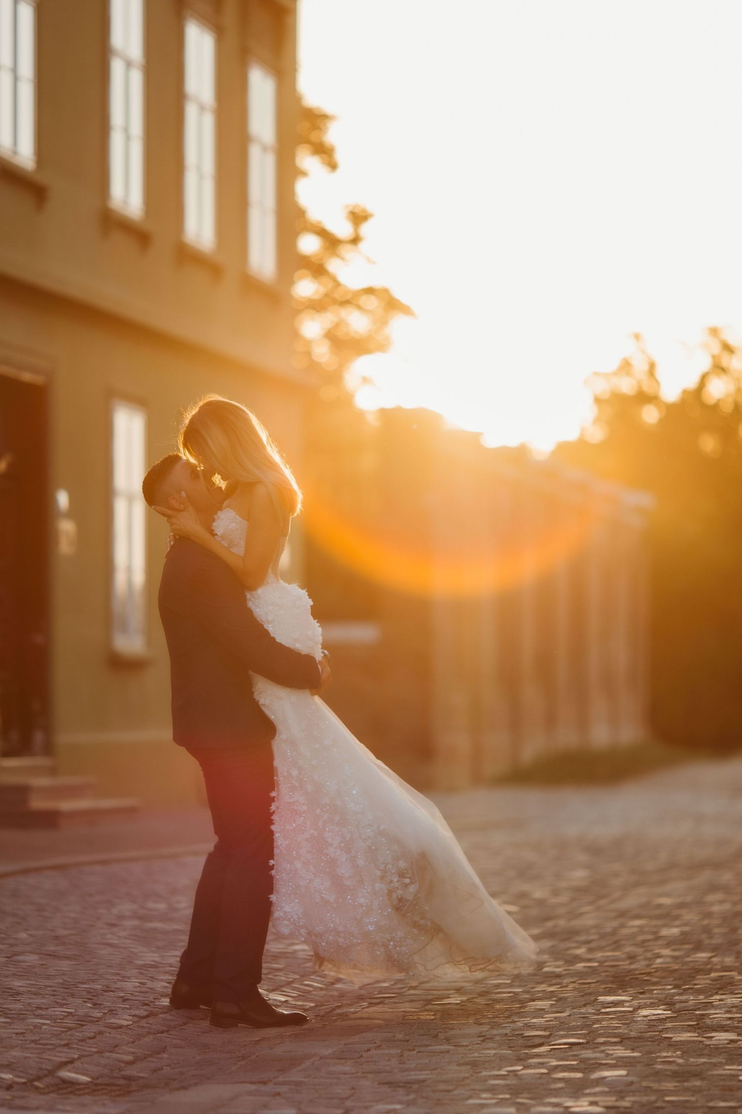 Wedding couple embraces on quiet cobblestone street during golden hour.