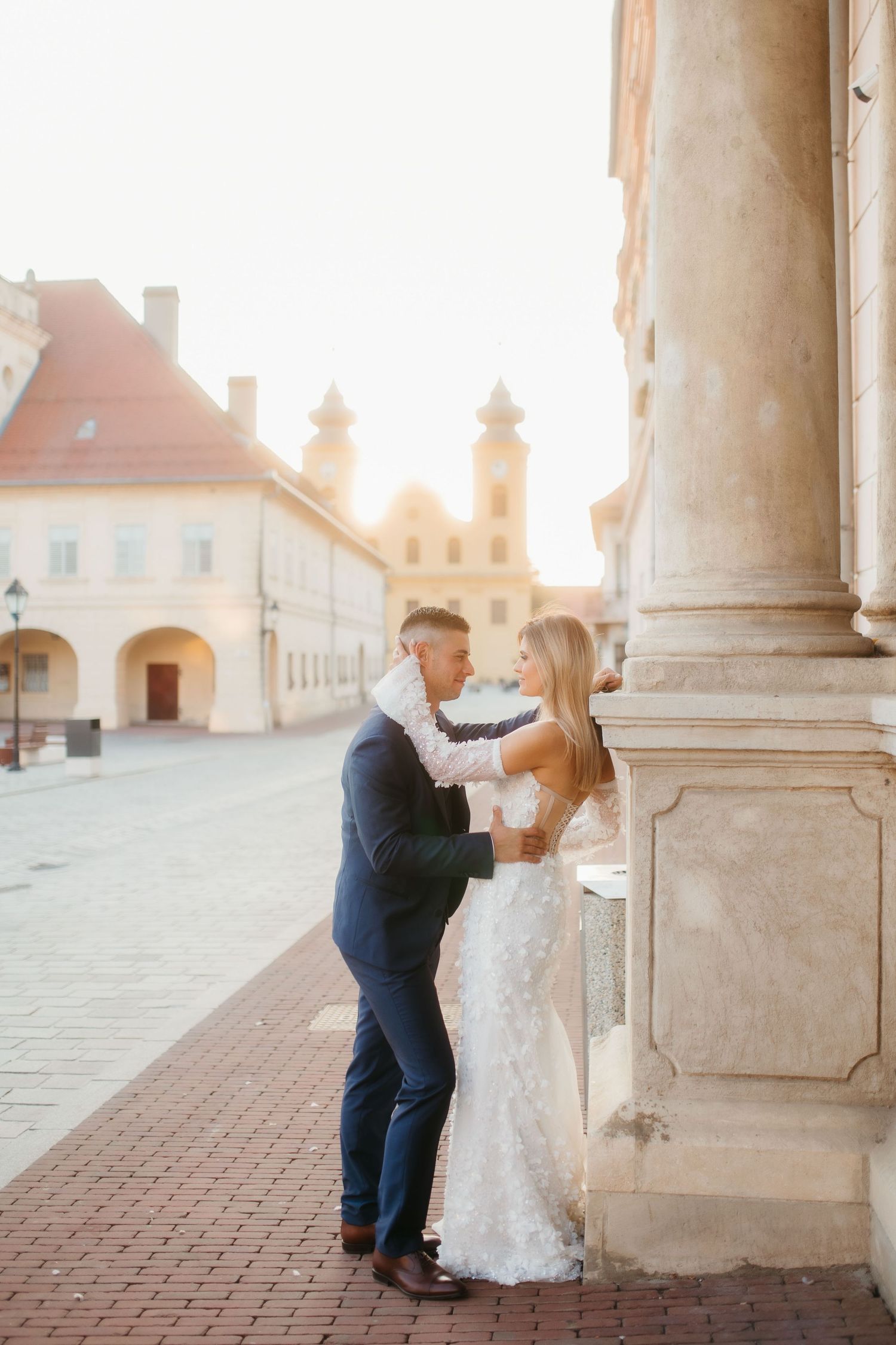Romantic wedding photo against historic building columns at sunset.