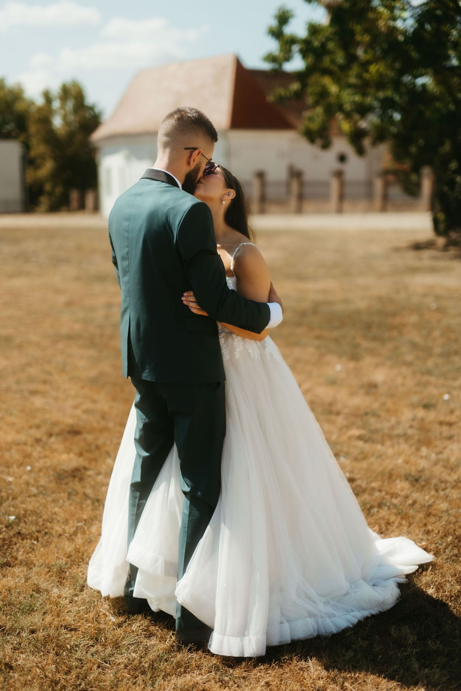 A couple shares an intimate moment on their wedding day, with the bride in white and groom in a dark suit outdoors.