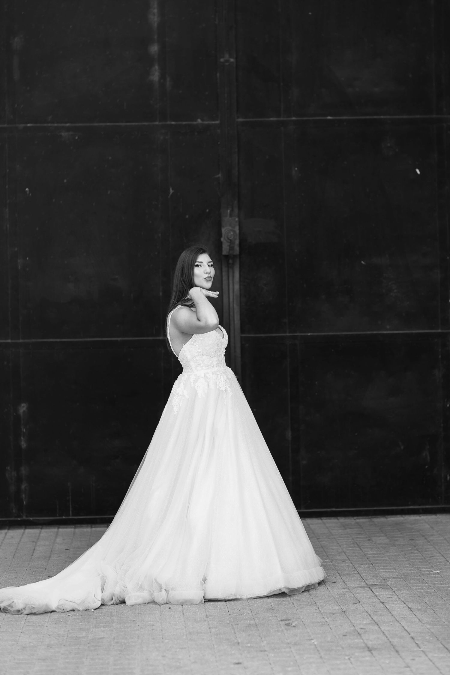 A flowing white wedding gown with tulle skirt creates an elegant silhouette against a dark background in this bridal portrait.