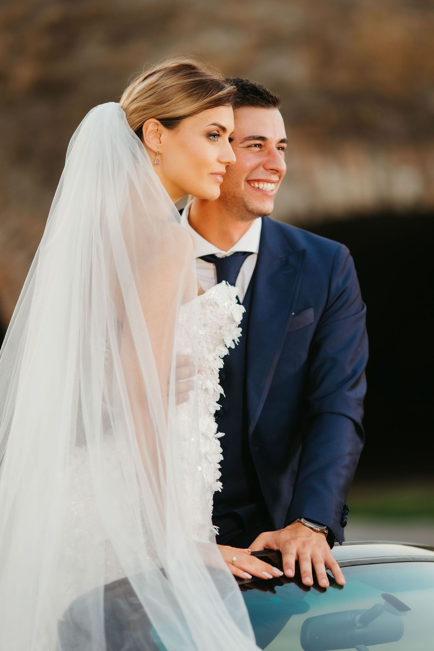 Intimate close-up wedding portrait against car with flowing white veil.
