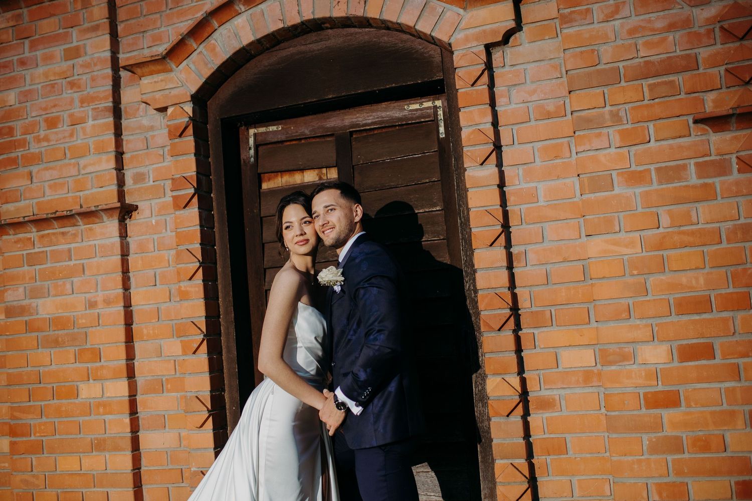 A couple embraces in front of a rustic brick wall during an intimate wedding photo session.