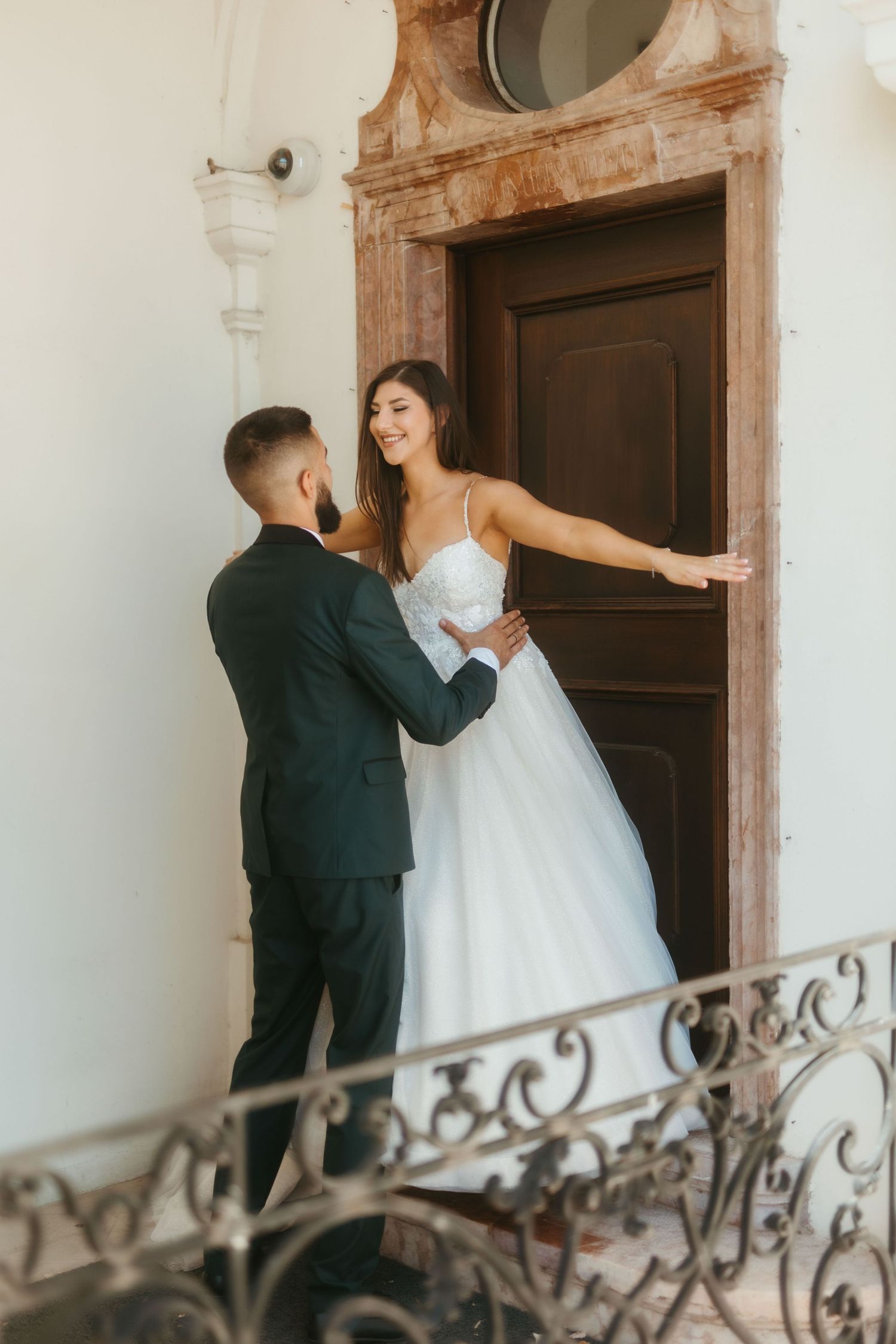 A couple in wedding attire share intimate moments on a staircase with ornate iron railings.