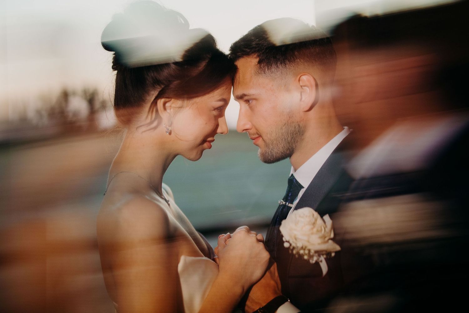 Intimate romantic moment between couple in casual wedding attire outdoors as sun sets behind them.