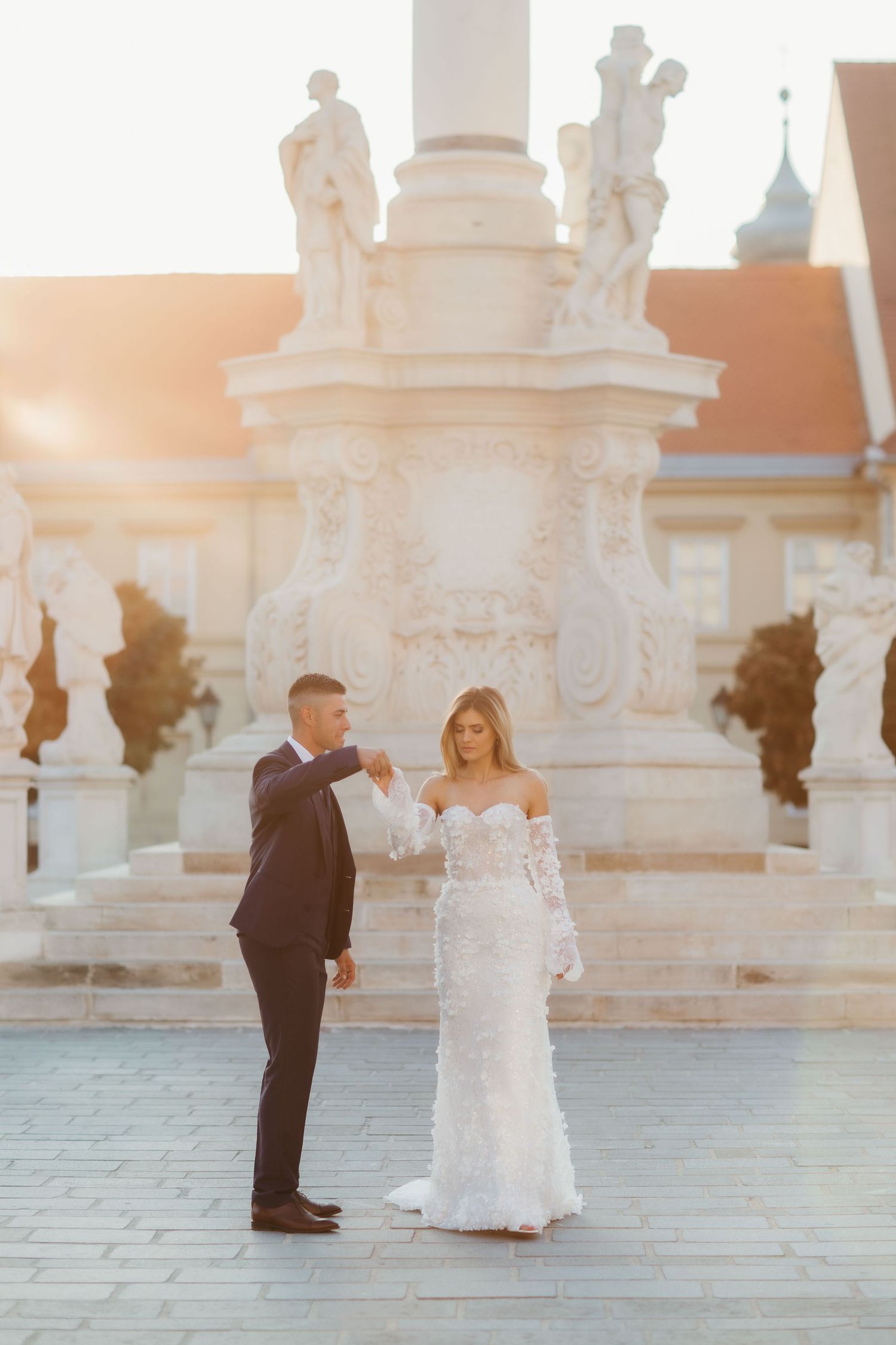 A romantic wedding photoshoot in front of an ornate white stone monument at sunset.