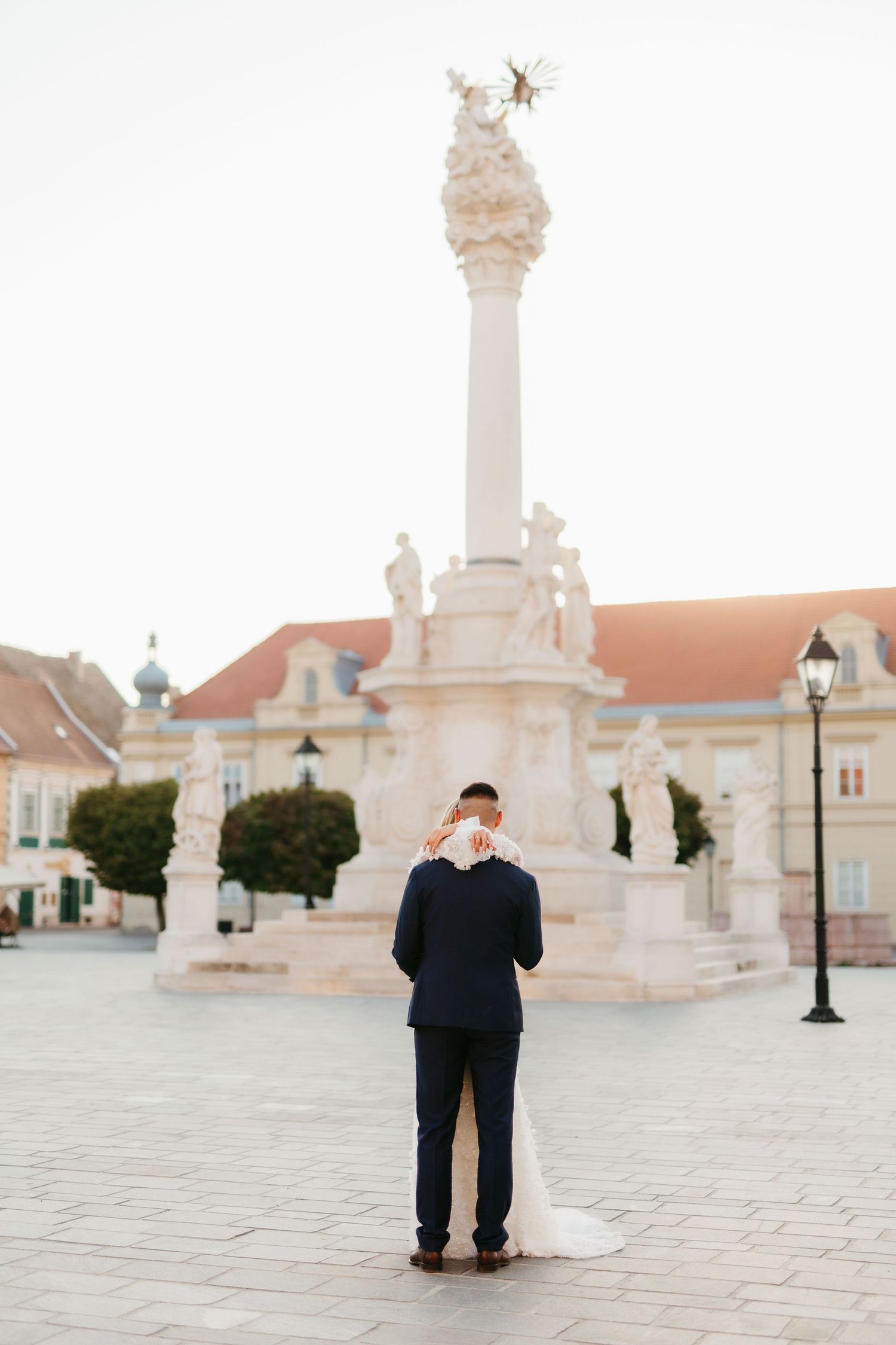 Person standing alone in front of ornate white monument and historic buildings.