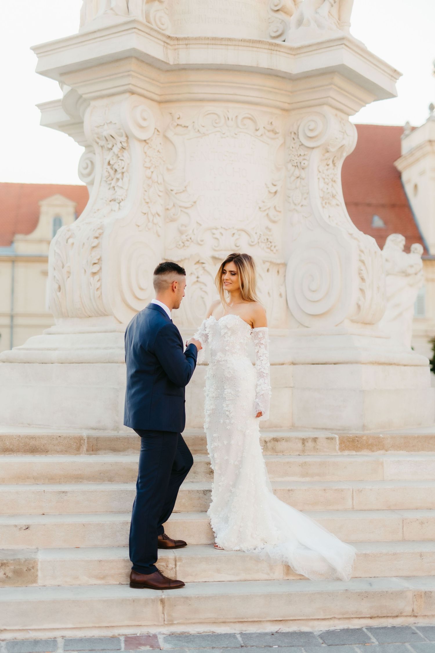Elegant wedding couple poses on stone steps by decorative white column.