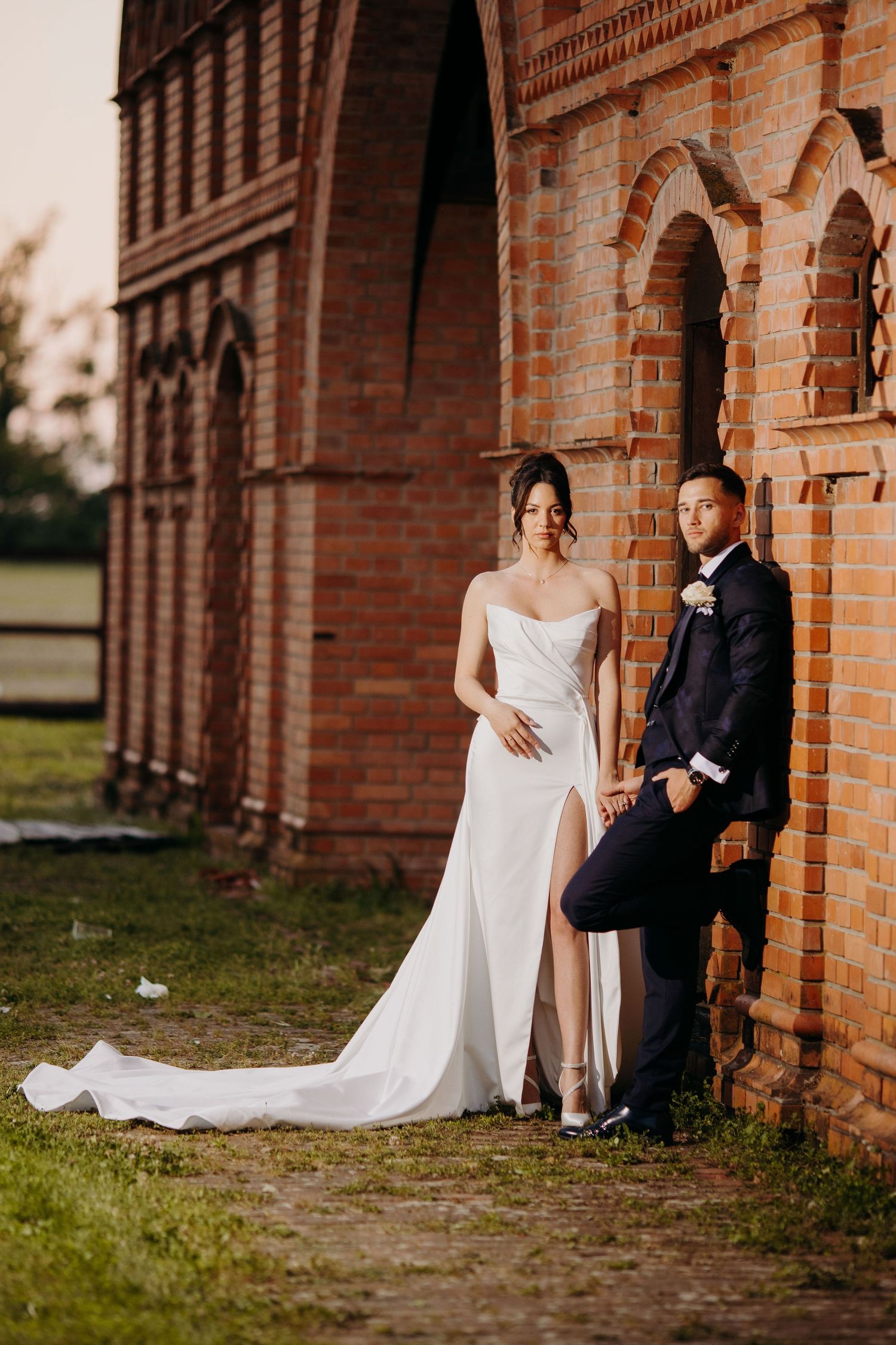 A bride and groom pose against a rustic brick archway during golden hour at their wedding.