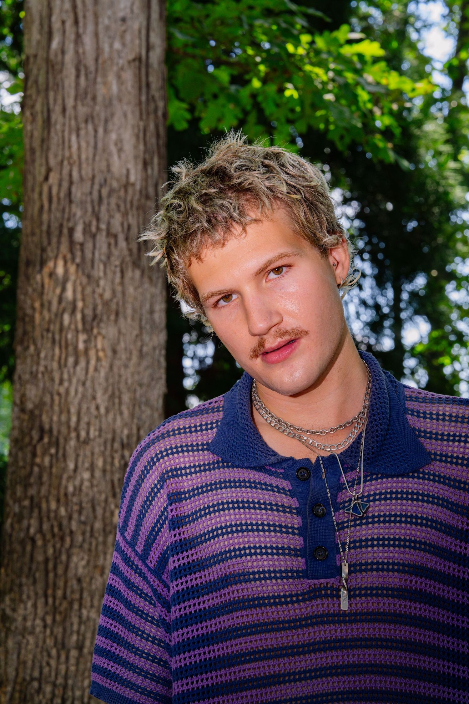 Casual outdoor portrait of person in striped polo against tree backdrop.