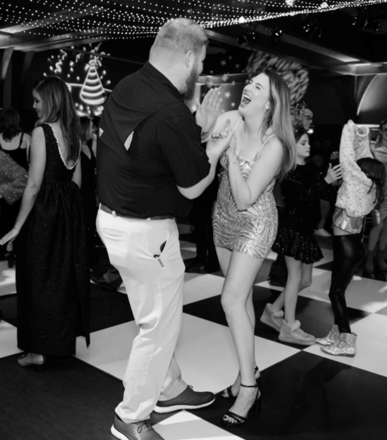 Black and white photo of dancing couple at party under string lights.