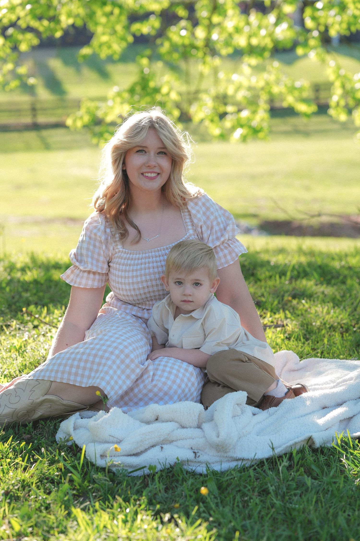Peaceful outdoor portrait on white blanket with gingham dress in sunlit garden setting.