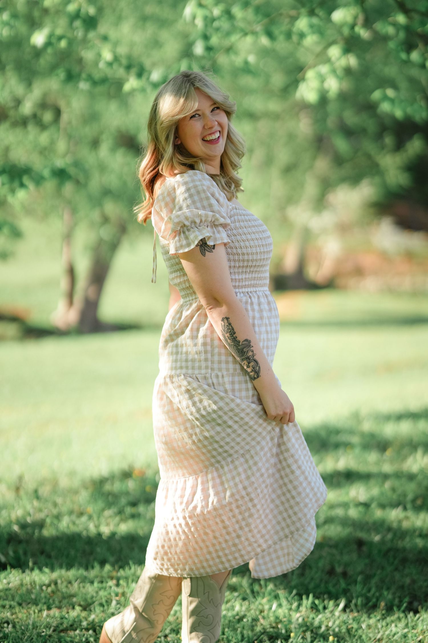 A joyful woman in a gingham dress twirls playfully in a sunlit garden setting.