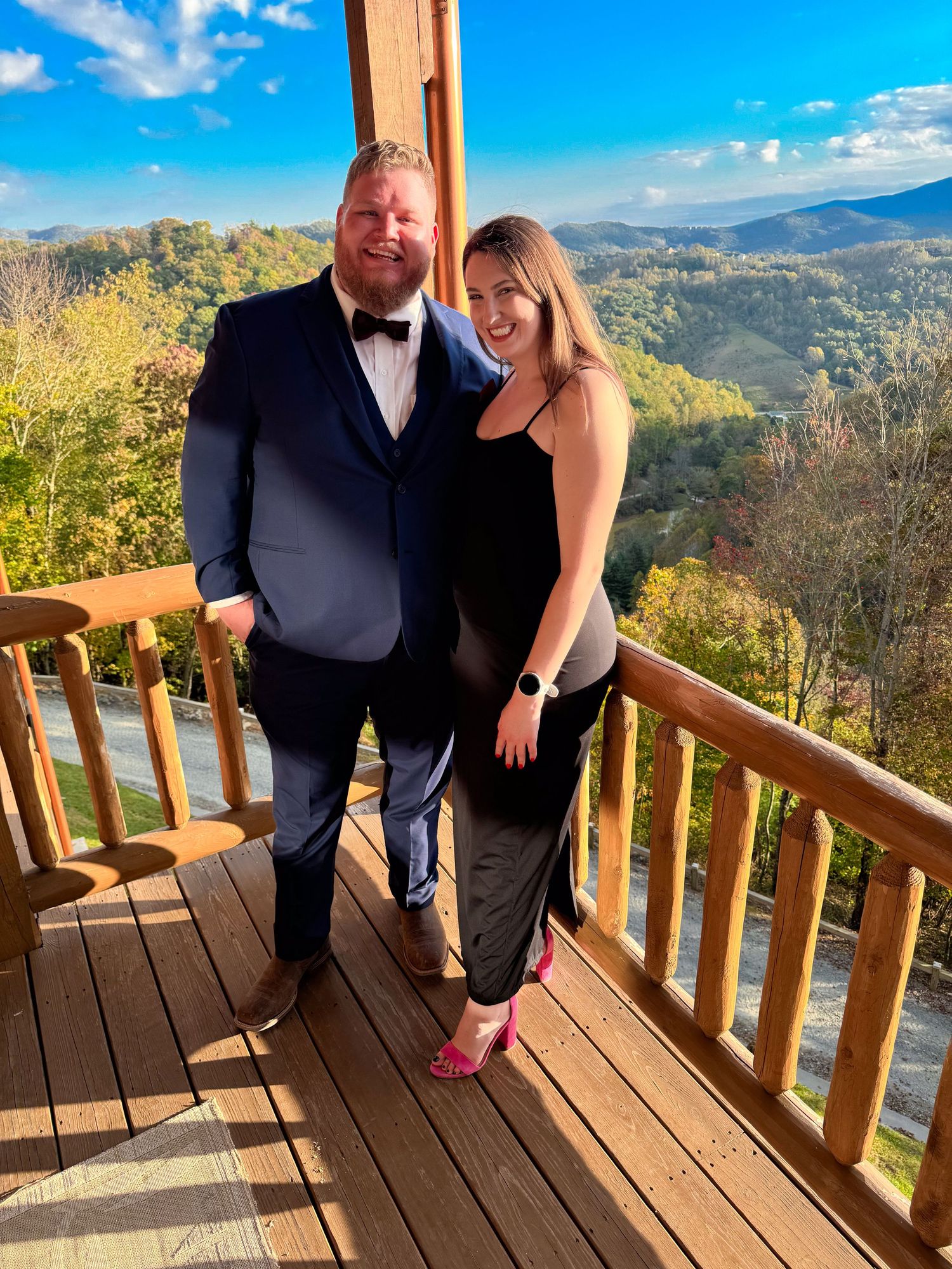 Couple posing on mountain deck with scenic fall foliage view in formal attire.